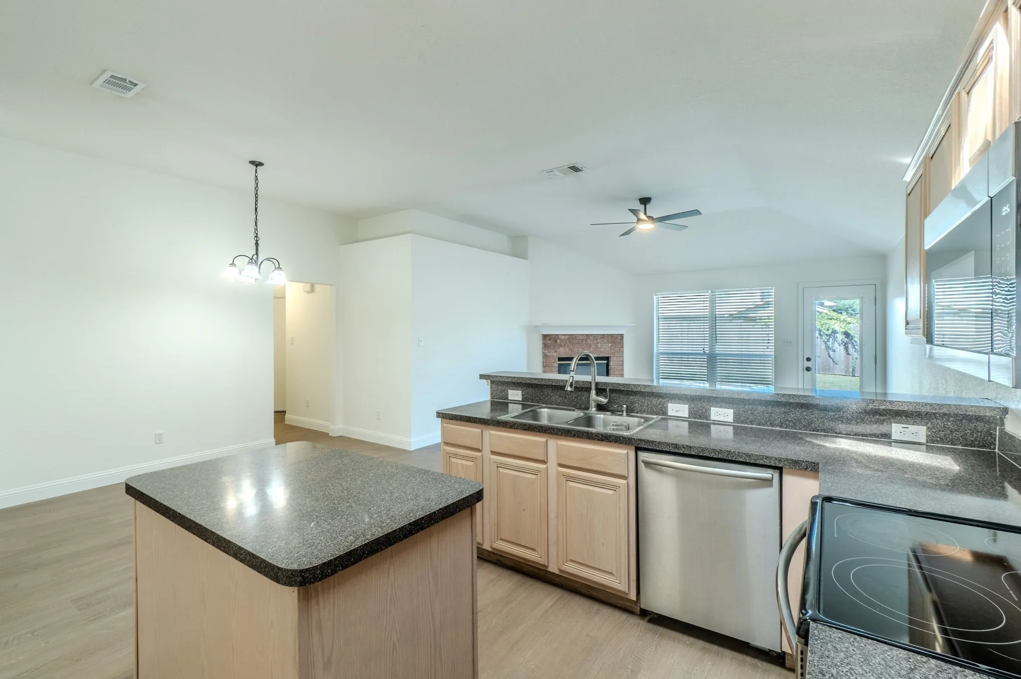Kitchen island with dark countertop, stainless steel dishwasher, double basin sink, and wood-finish cabinetry