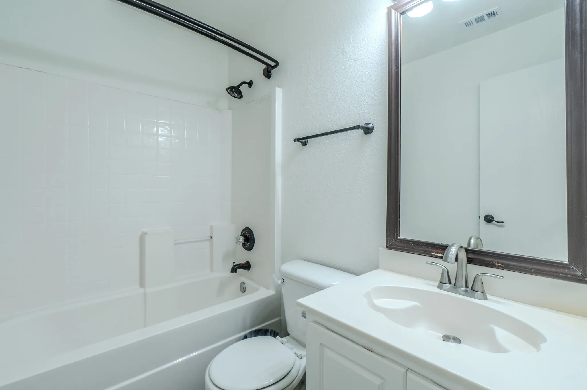 Bathroom with a built-in tub and shower combination, white subway tile surround, dark bronze fixtures, and a vanity with a white countertop and integrated sink