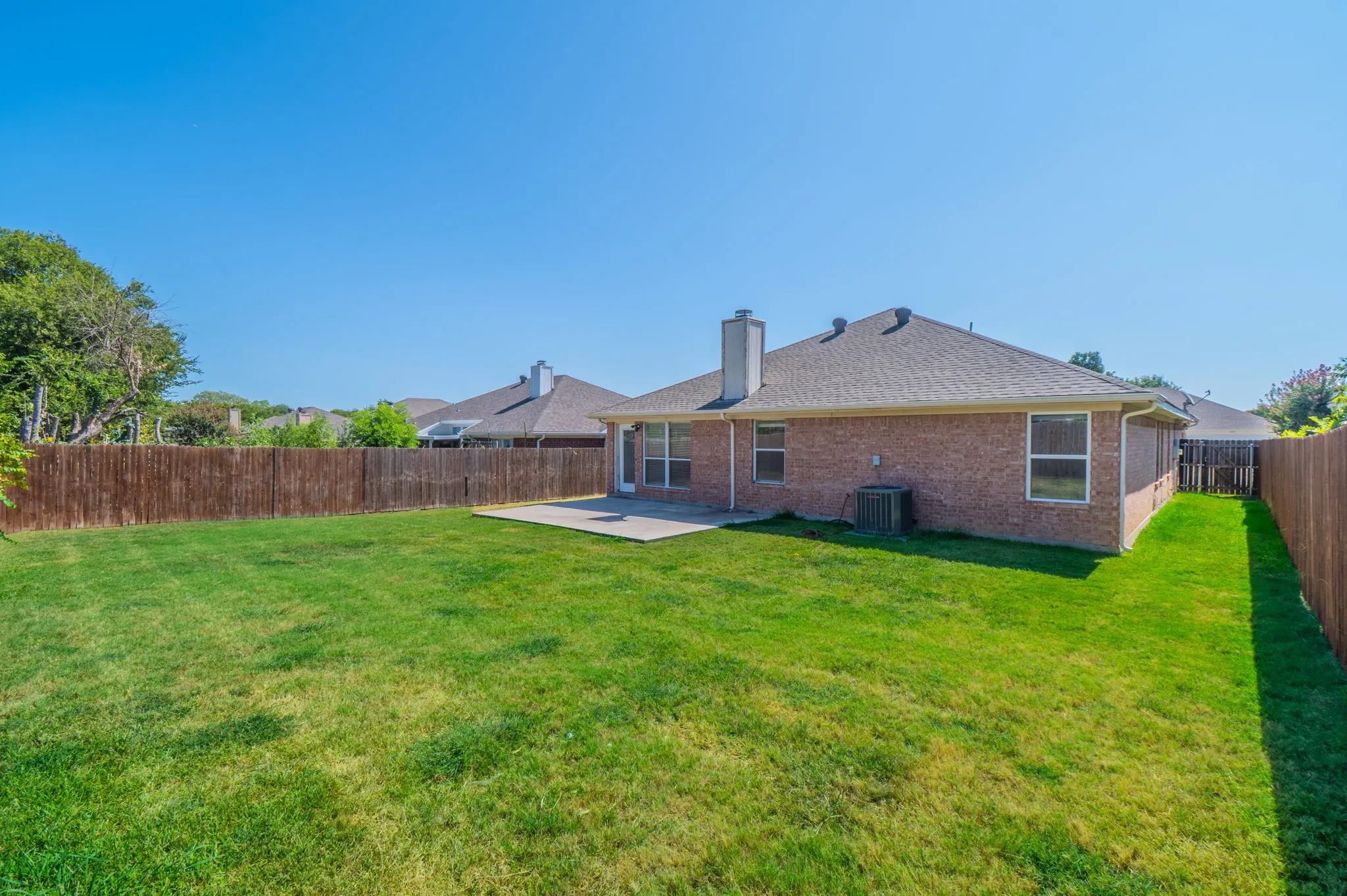 Expansive backyard with a manicured lawn, full wood privacy fencing, and a concrete patio