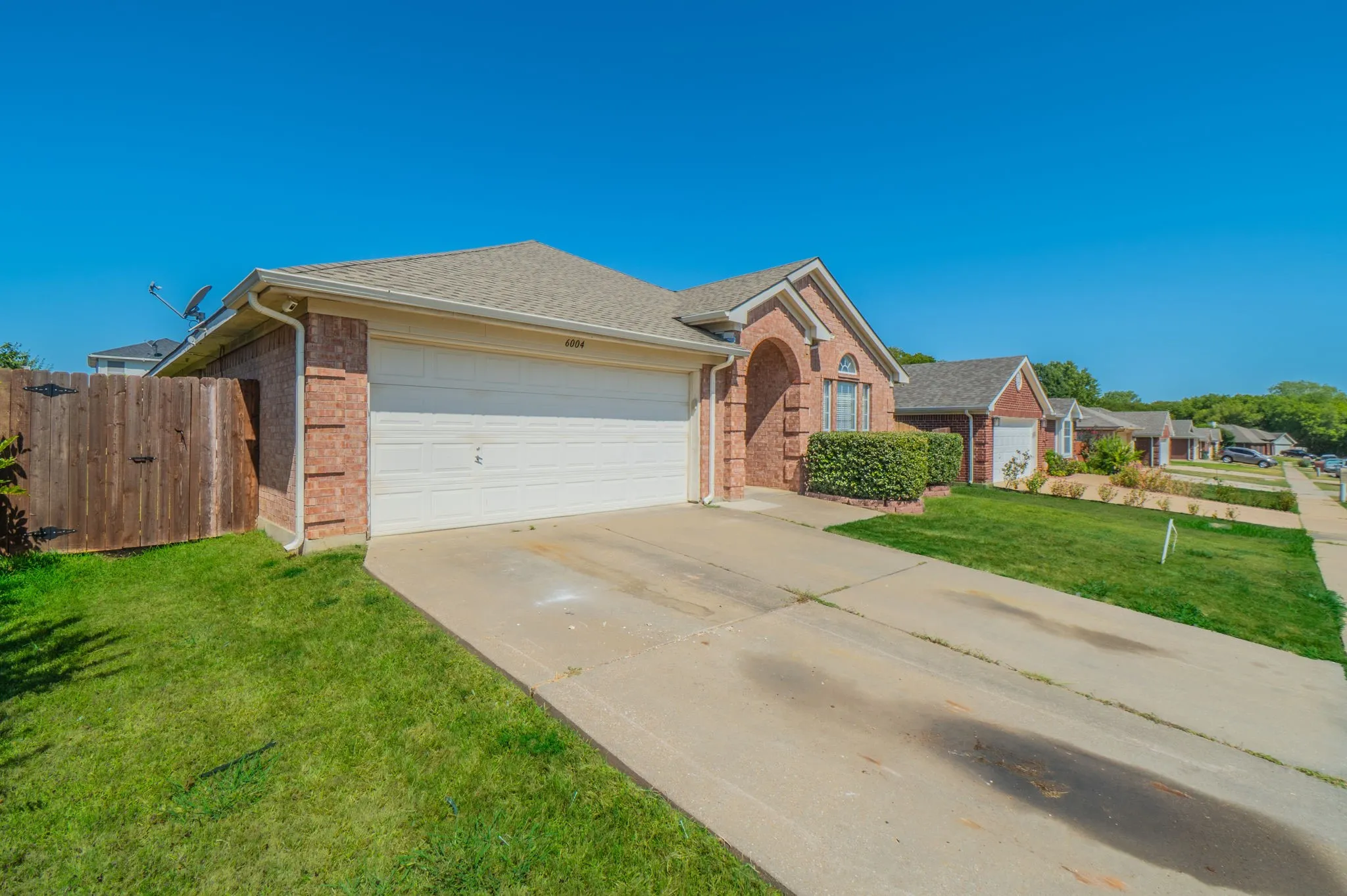 Brick exterior with an attached garage, paved driveway, and established landscaping