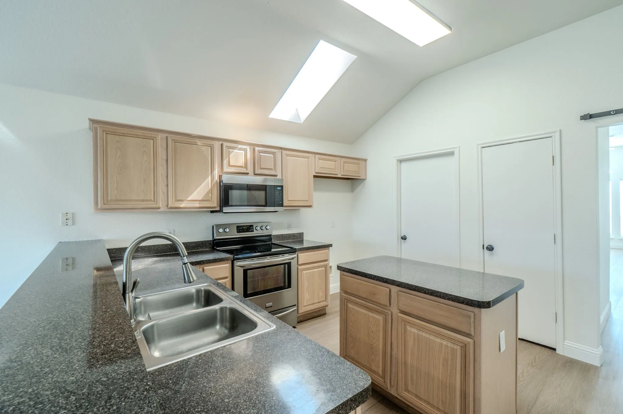 Kitchen featuring stainless steel appliances, dual skylights, a center island with countertop, a dual-basin sink, and wood-finish flooring