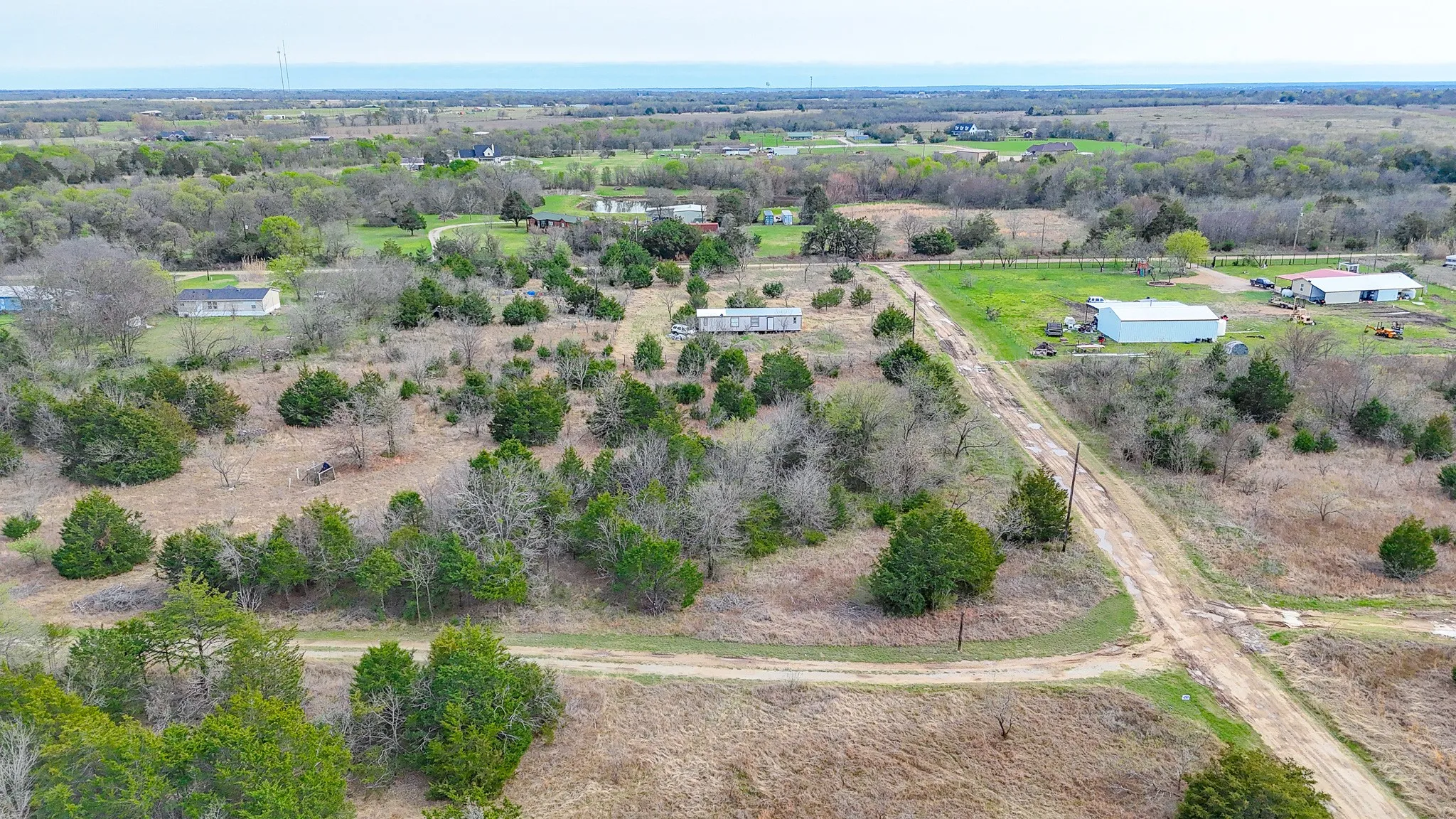 Expansive rural property featuring a dirt road, scattered trees, and distant structures