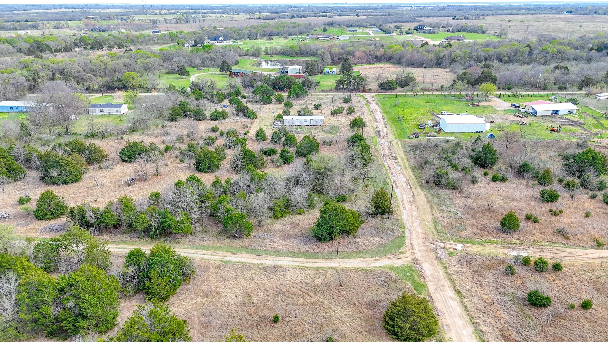 Expansive land featuring natural tree coverage, open clearings, and existing structures