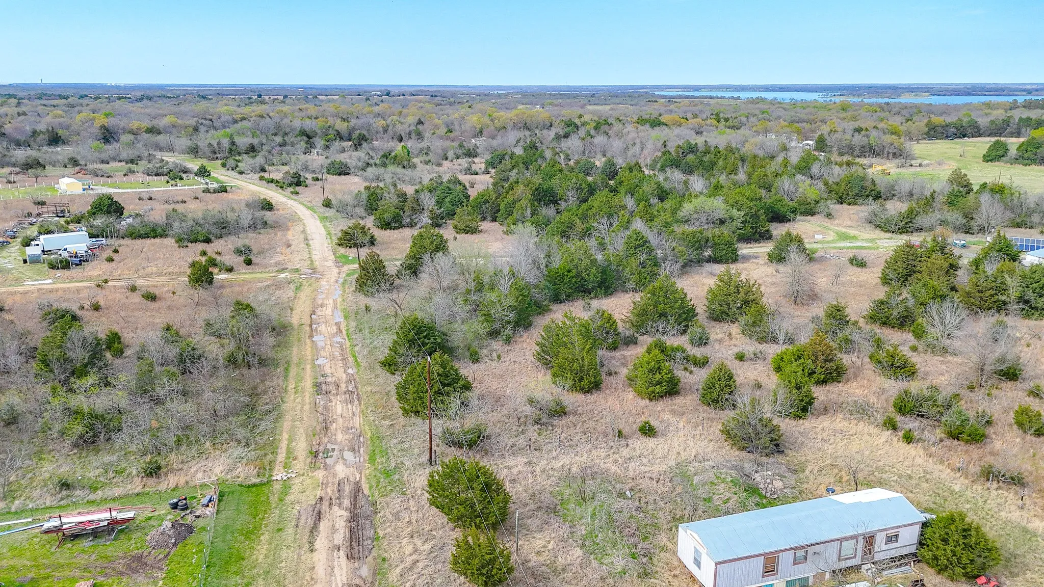 Aerial perspective showcasing expansive natural landscape with a gravel road, abundant mature trees, and distant water feature