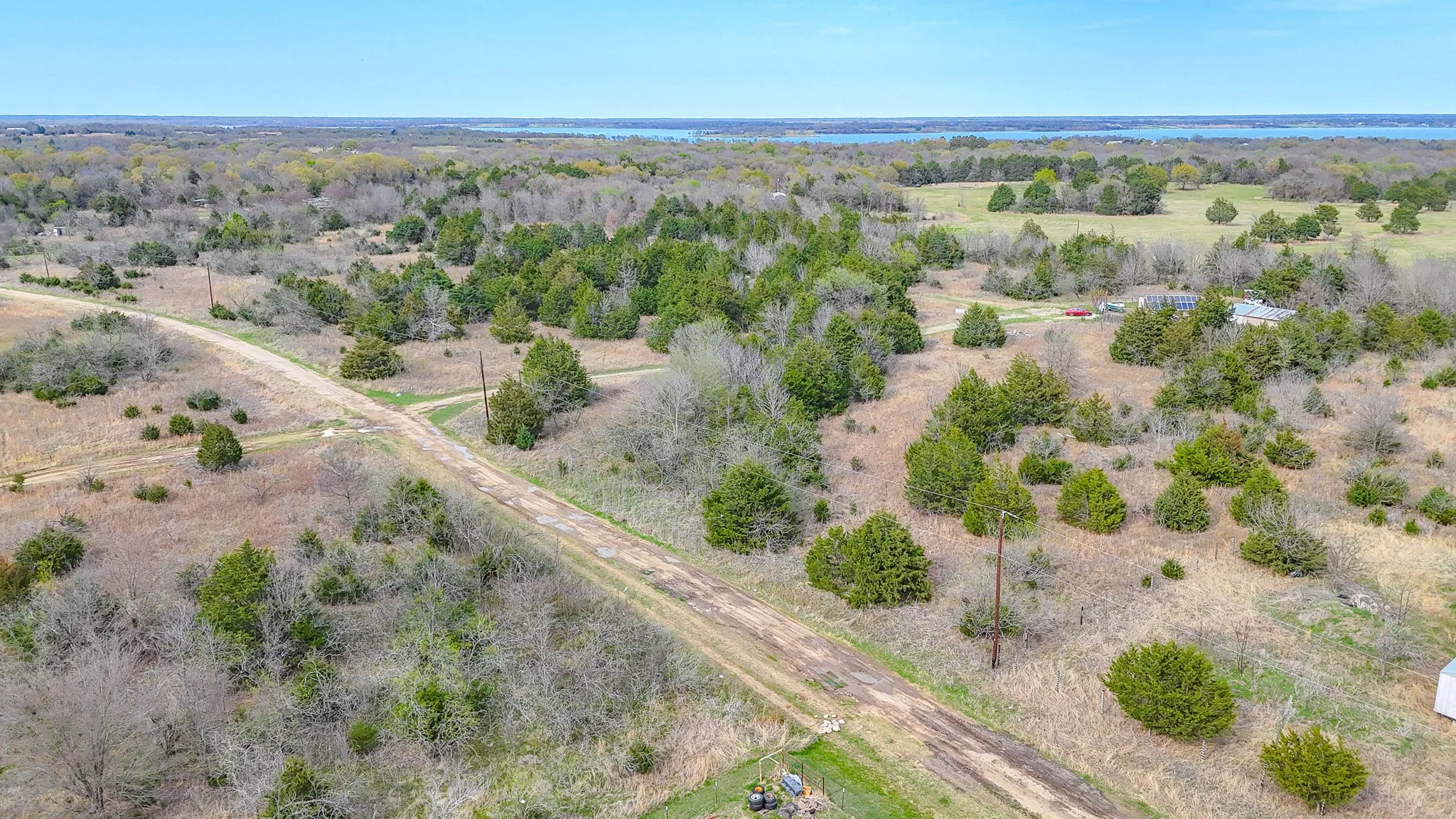 Expansive rural landscape with a distant body of water, scattered trees, and an unpaved access road