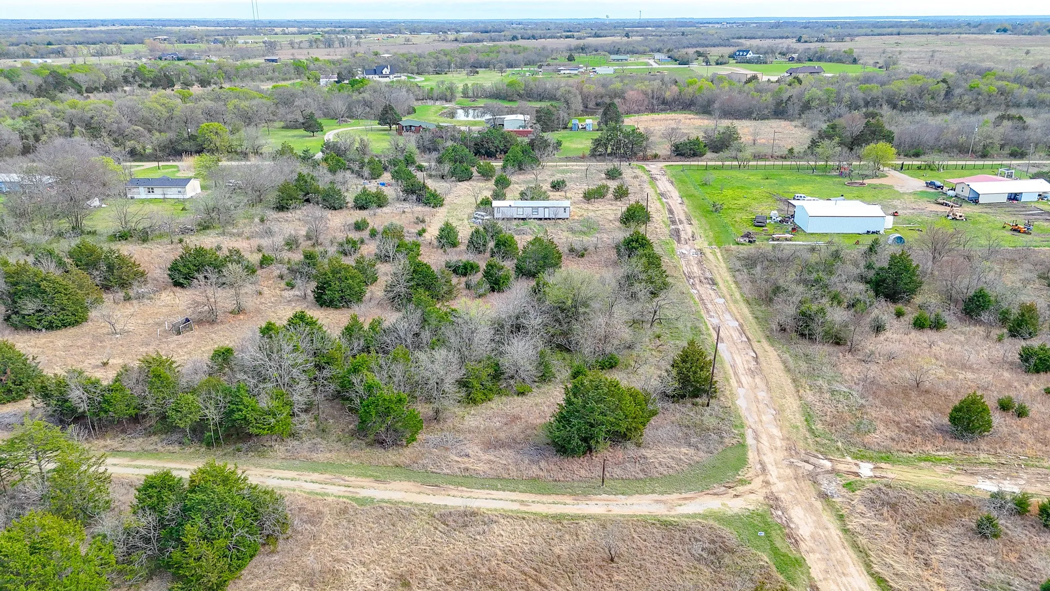 Expansive land parcel featuring open fields, scattered mature trees, and an established unpaved access road