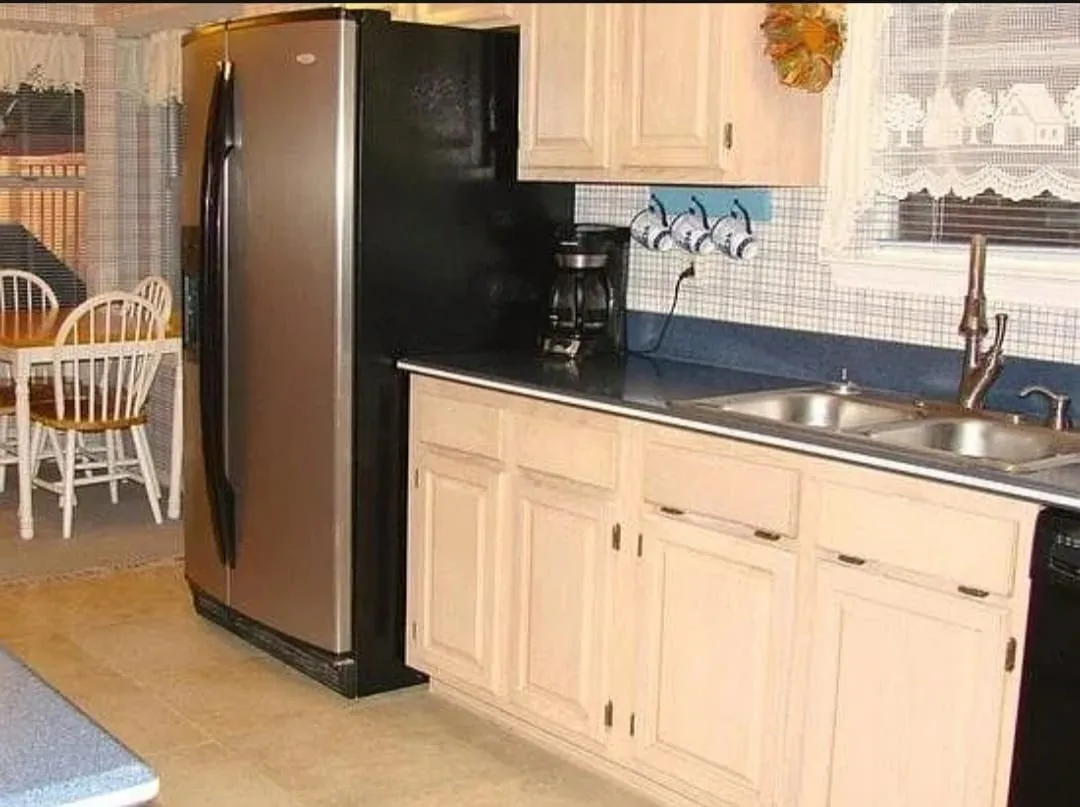 Kitchen featuring wood-finish flooring, light-toned cabinetry, a stainless steel refrigerator, a double basin sink, and a tiled backsplash
