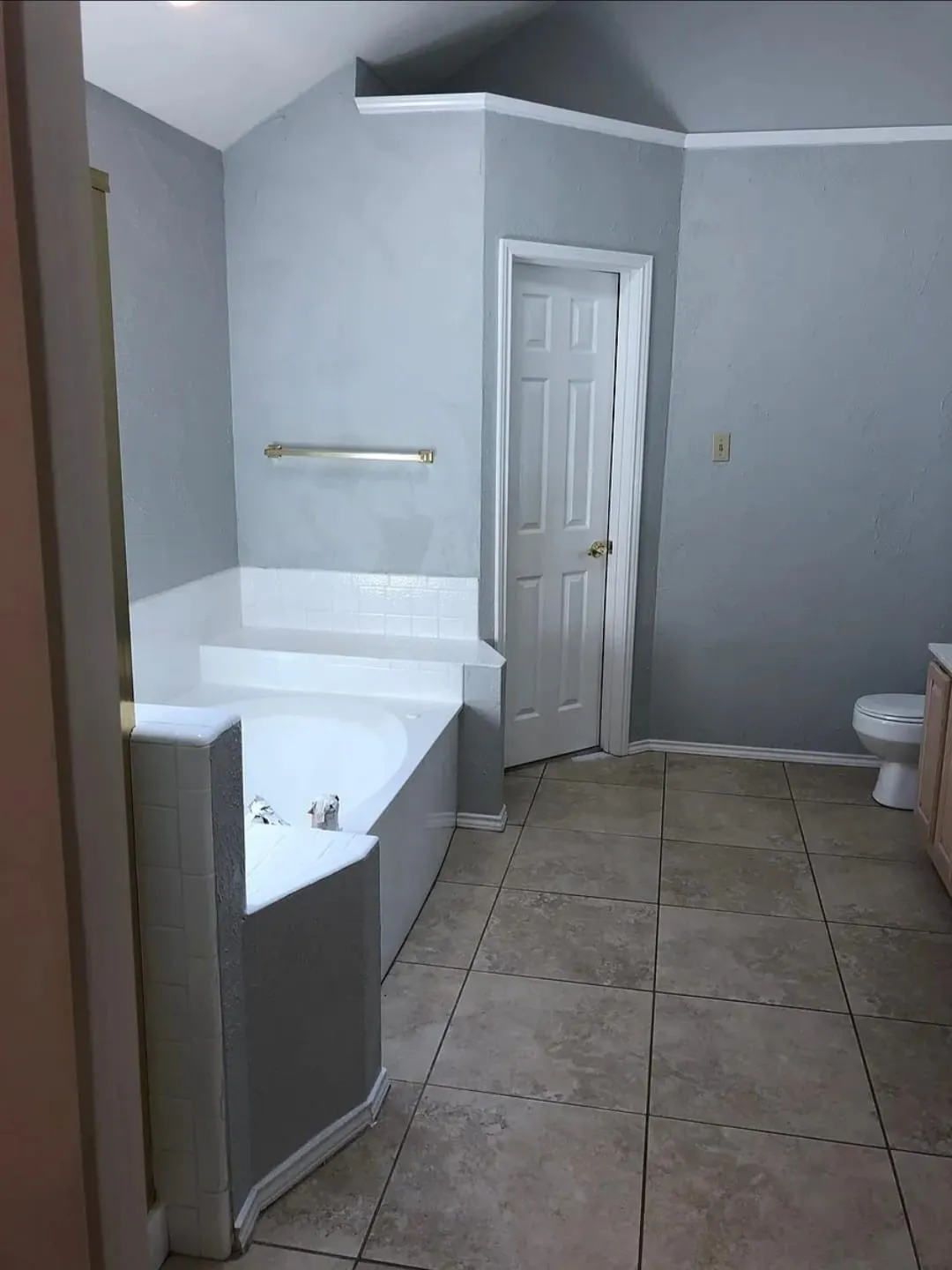 Built-in corner tub with tiled surround, light-toned floor tile, and white paneled door