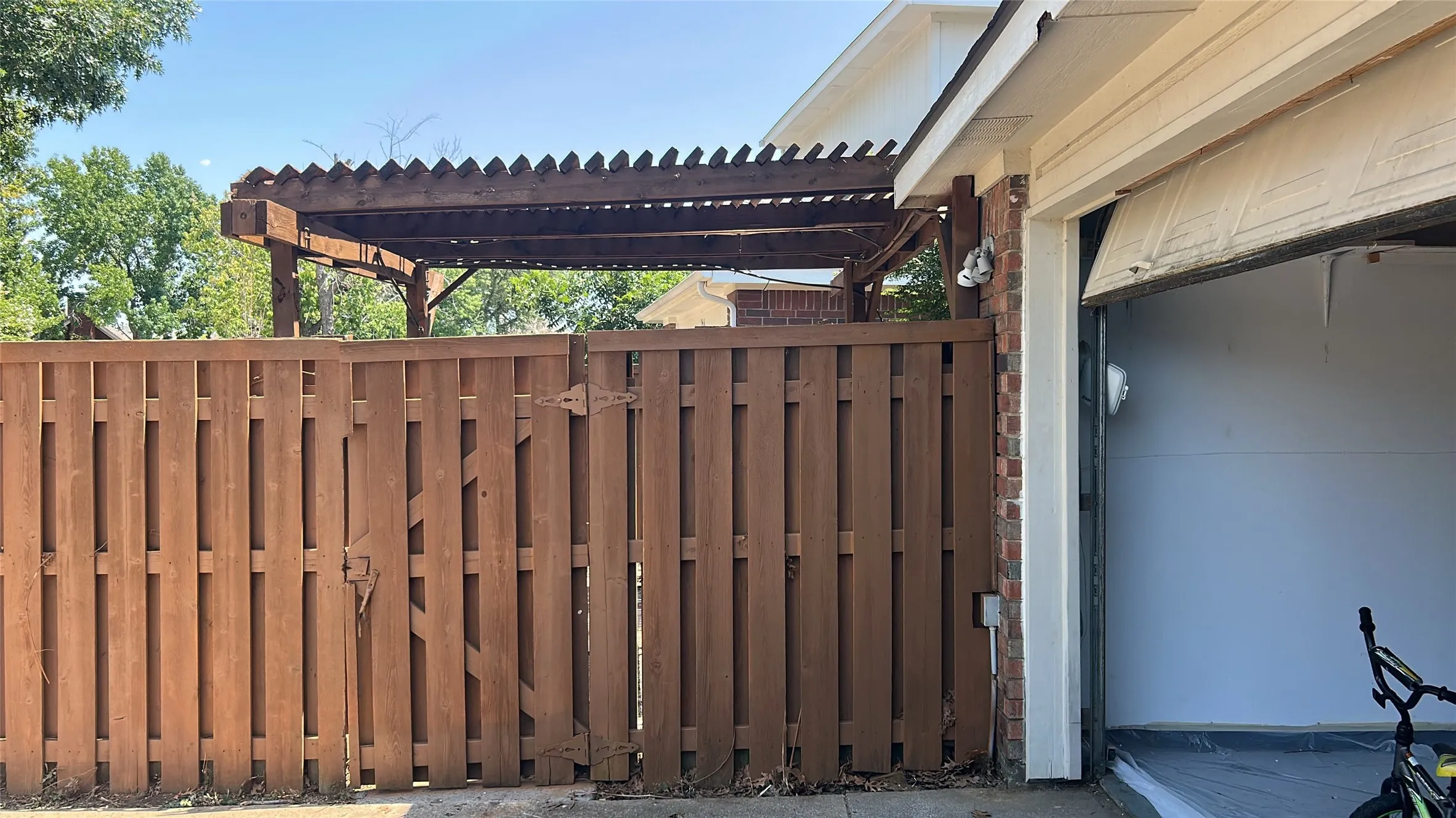 Wood privacy fence with gate, wood pergola, brick exterior, and attached garage