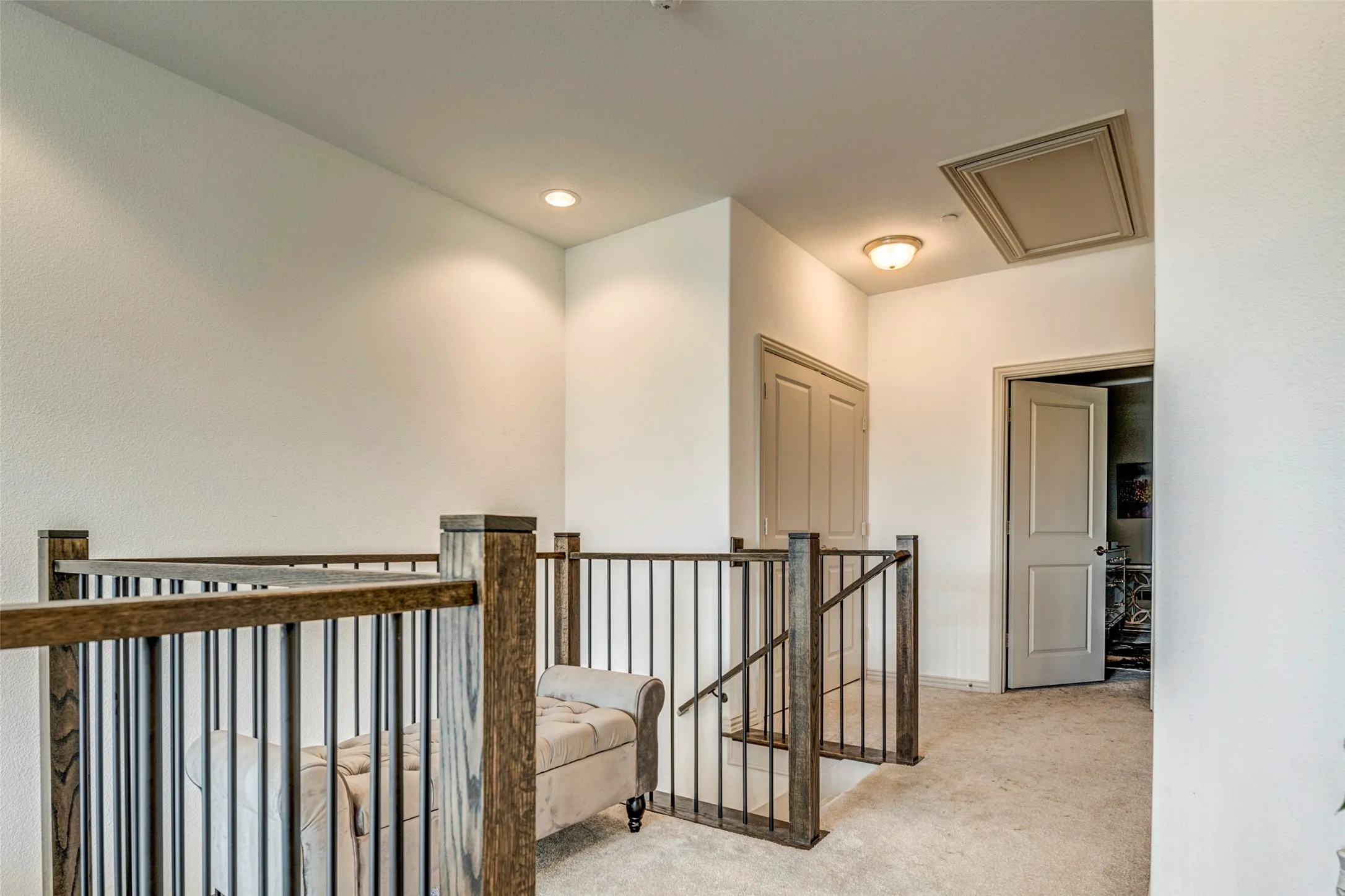 Upper-level landing featuring wood-finish railings with black iron balusters, recessed lighting, a flush-mount light fixture, and neutral carpeting