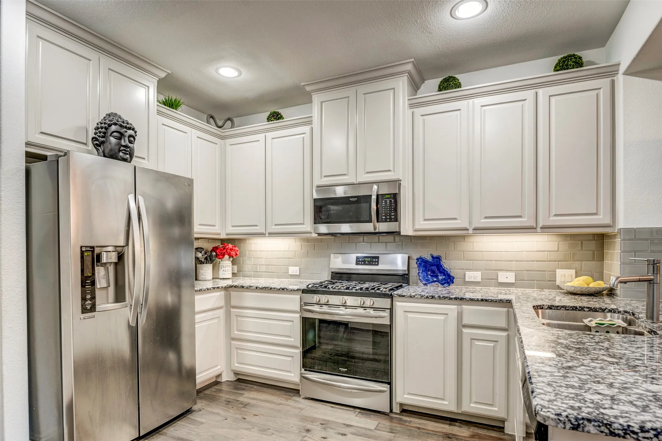 Kitchen featuring white cabinetry, granite countertops, stainless steel appliances, a tiled backsplash, and wood-finish flooring