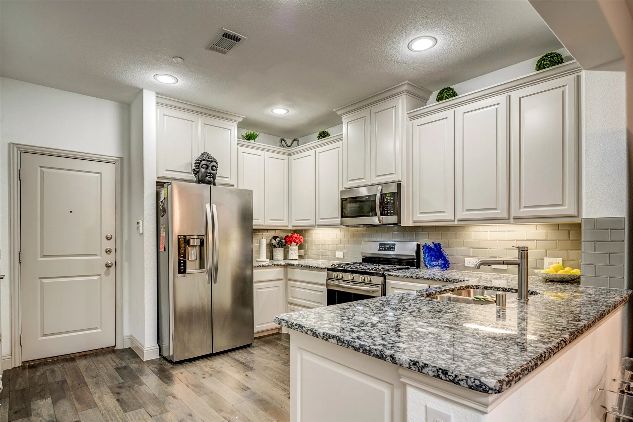 Gourmet kitchen with white cabinetry, stainless steel appliances, speckled stone countertops, a subway tile backsplash, and wood-finish flooring