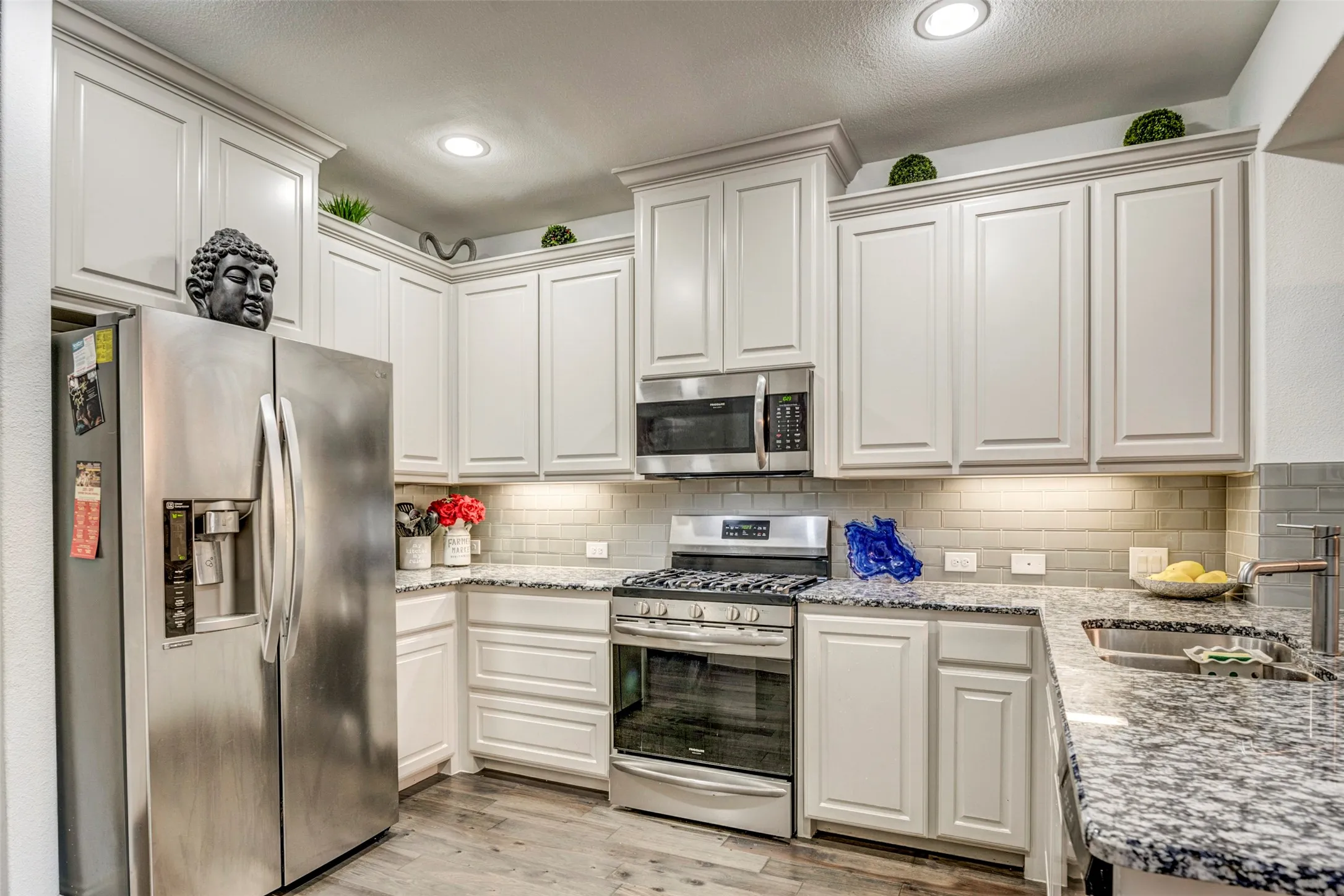 Well-appointed kitchen featuring light-toned cabinetry, stainless steel appliances, speckled stone countertops, a subway tile backsplash, and recessed lighting