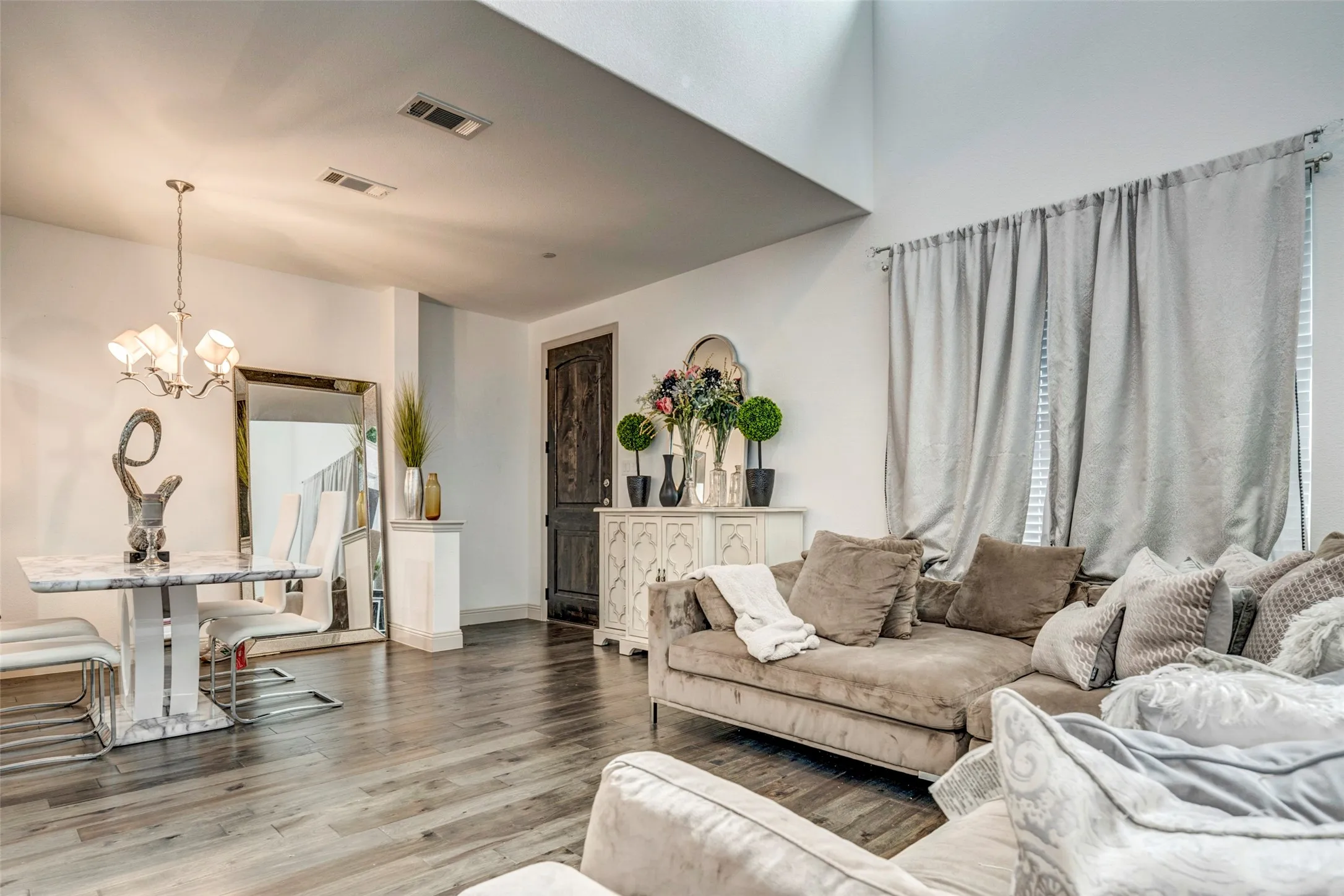 Open-concept living space featuring wood-finish flooring, high ceilings, and a decorative entry door