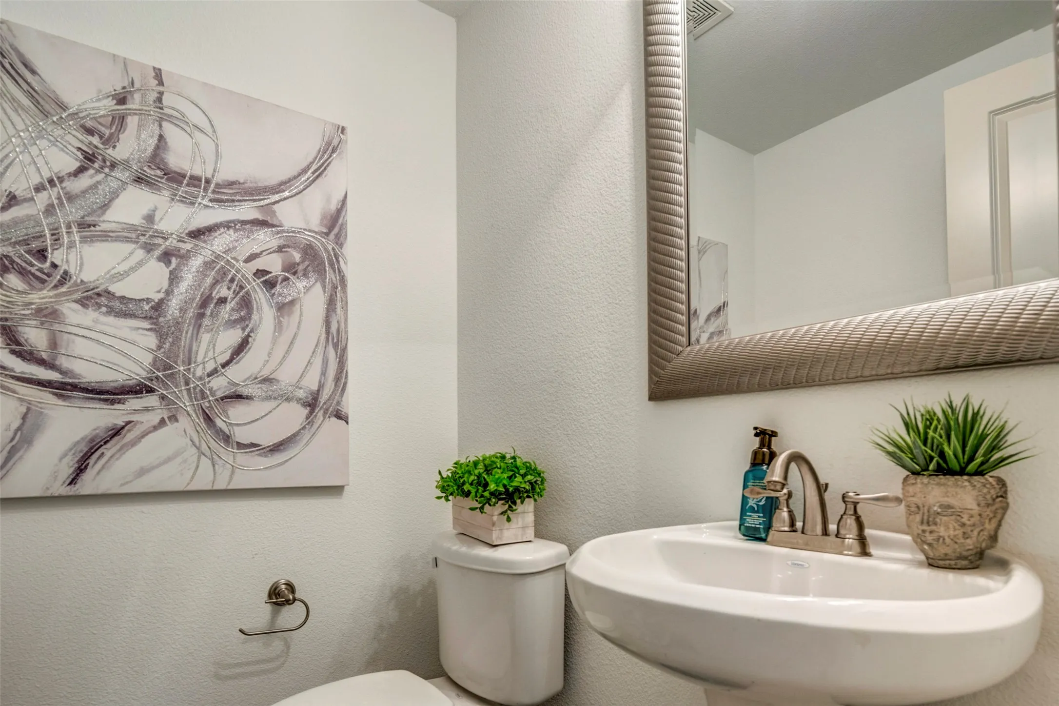 Elegant powder room featuring a curved pedestal sink with brushed nickel faucet, framed mirror with decorative molding, and soft neutral walls