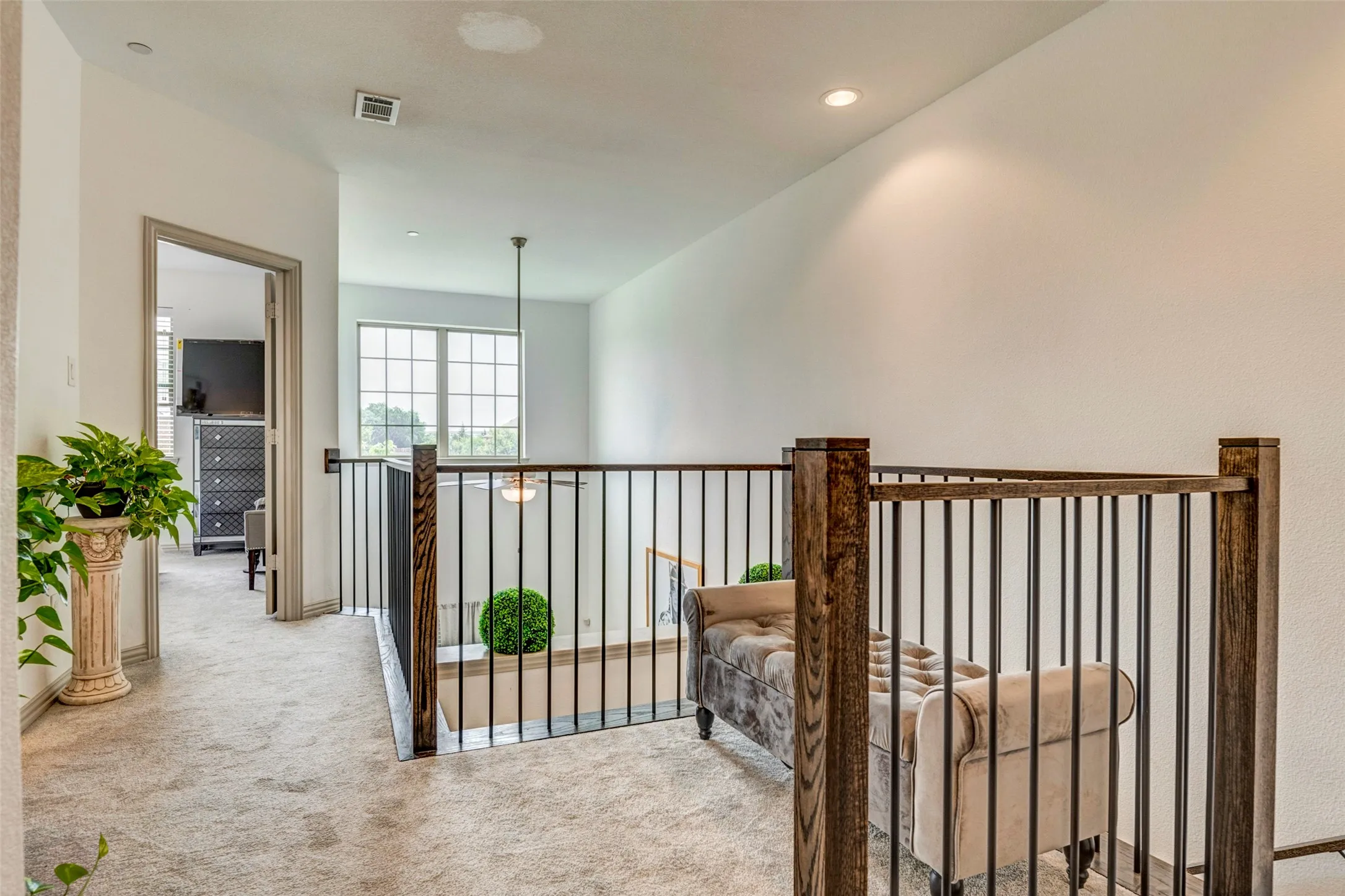 Upper-level hallway featuring light-colored carpeting, a dark wood-finish and metal baluster railing system, and recessed lighting