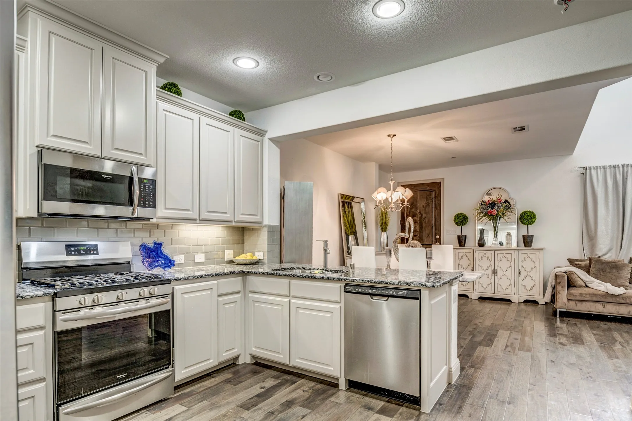 Open-concept kitchen featuring white cabinetry, stainless steel appliances, granite countertops, tile backsplash, and wood-finish flooring