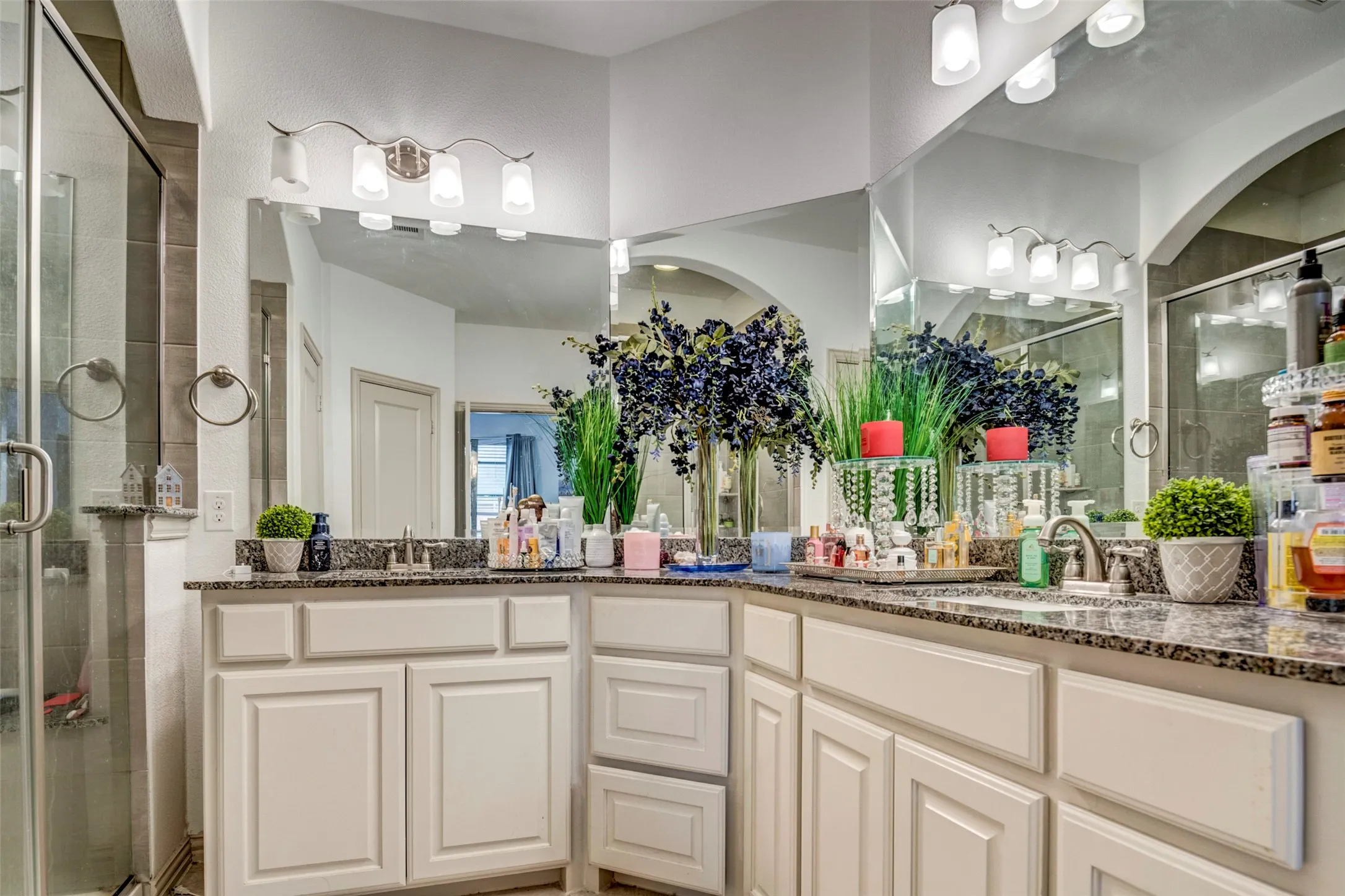 Double vanity with granite countertops, integrated sinks, white cabinetry, and a full-width mirror