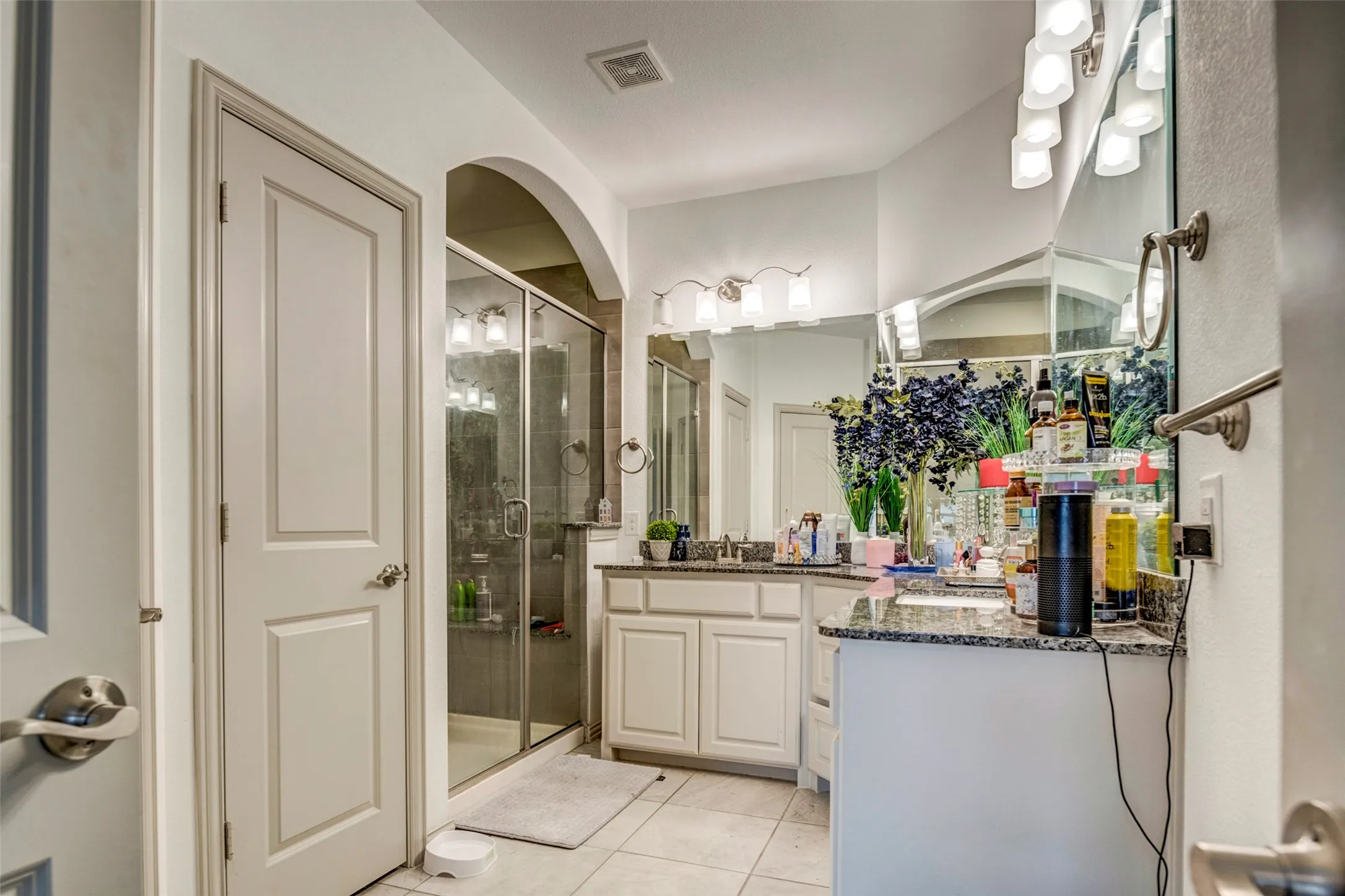 Bathroom featuring a frameless glass shower enclosure, dual vanity with undermount sinks, granite countertops, and tiled flooring