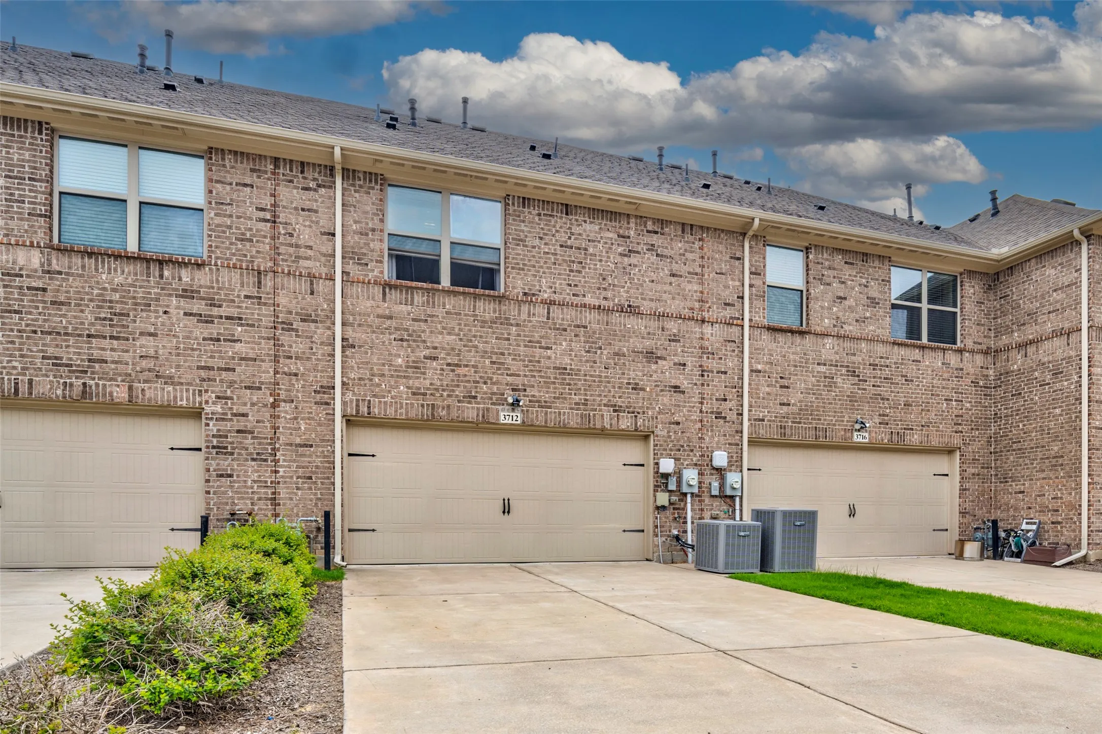 Brick exterior with individual garage access and an asphalt shingle roof