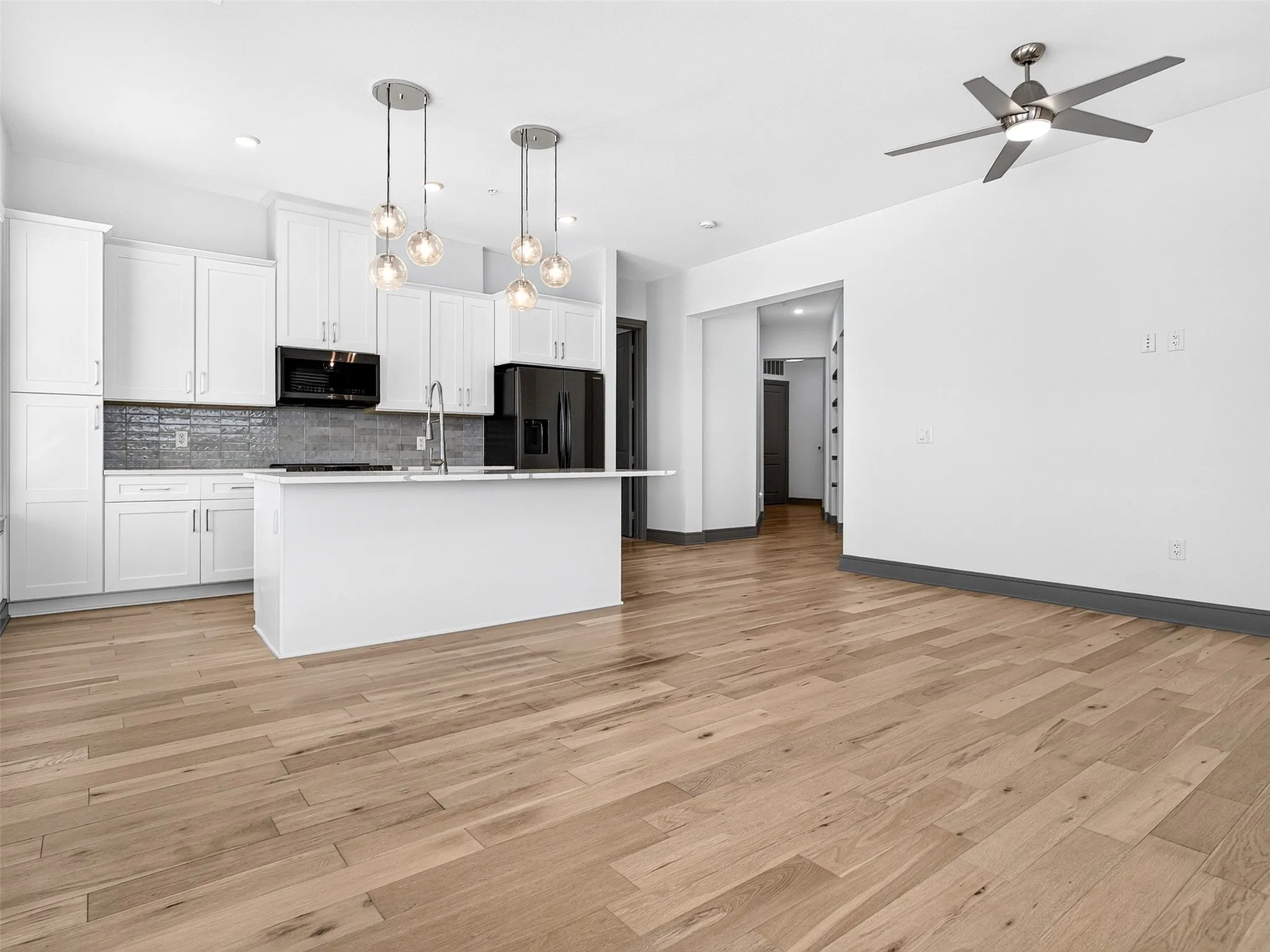 Open-concept living space with light wood-finish flooring, white walls, and a modern ceiling fan