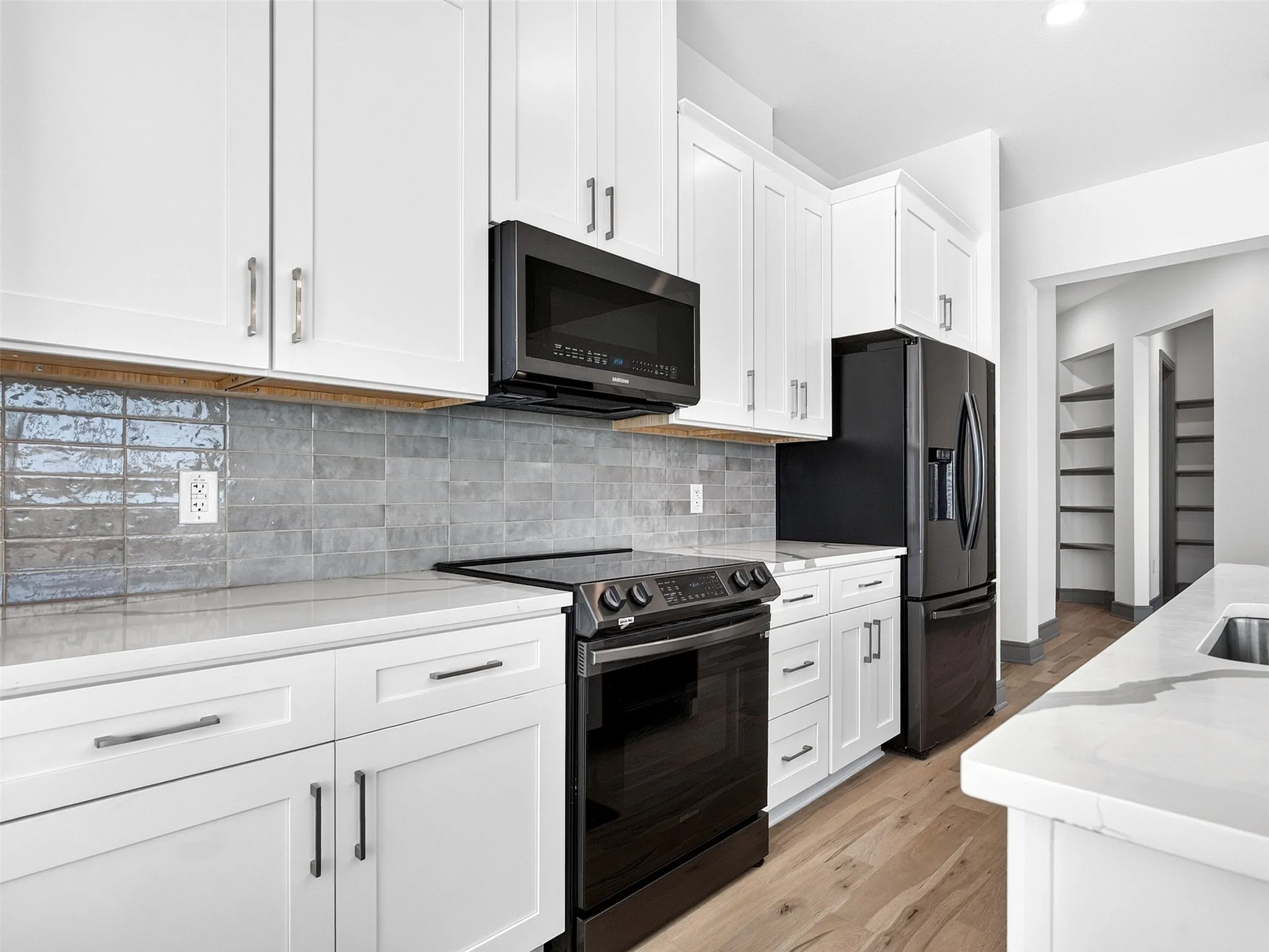 White shaker cabinetry, black stainless steel appliances, stone countertops, gray subway tile backsplash, and wood-finish flooring