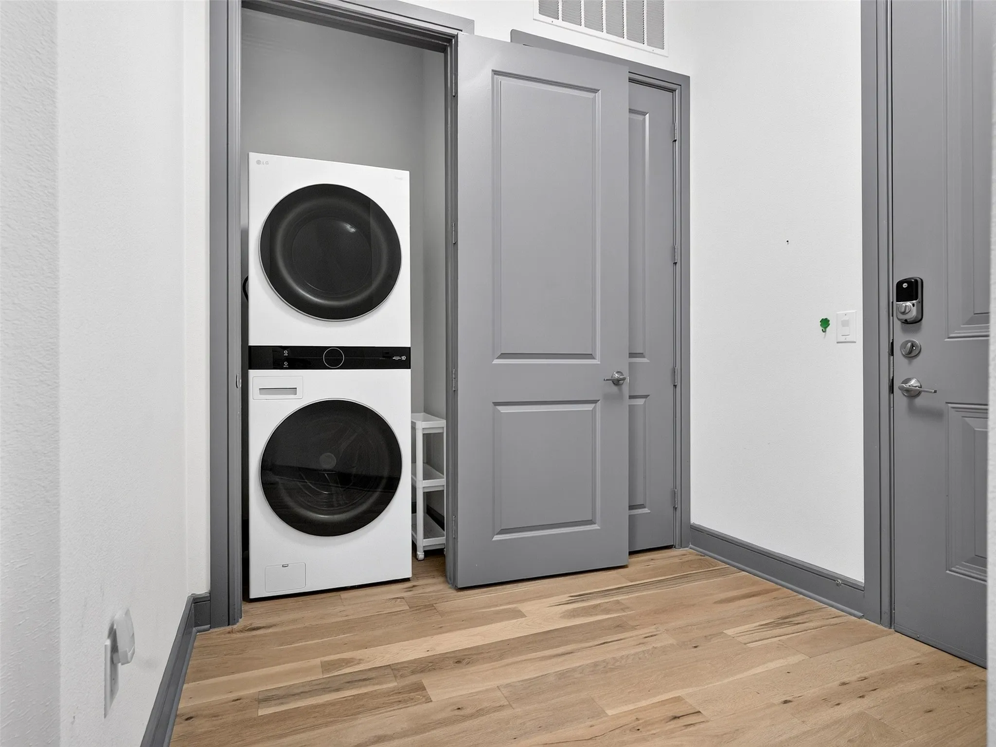 Stackable washer and dryer unit, light wood-finish flooring, white walls, and gray trim