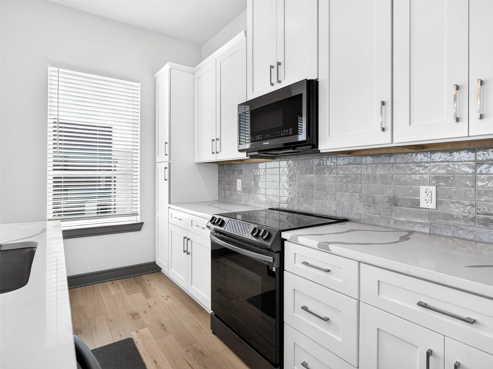 White cabinetry, quartz countertops with gray veining, black built-in microwave, black electric range, and wood-finish flooring