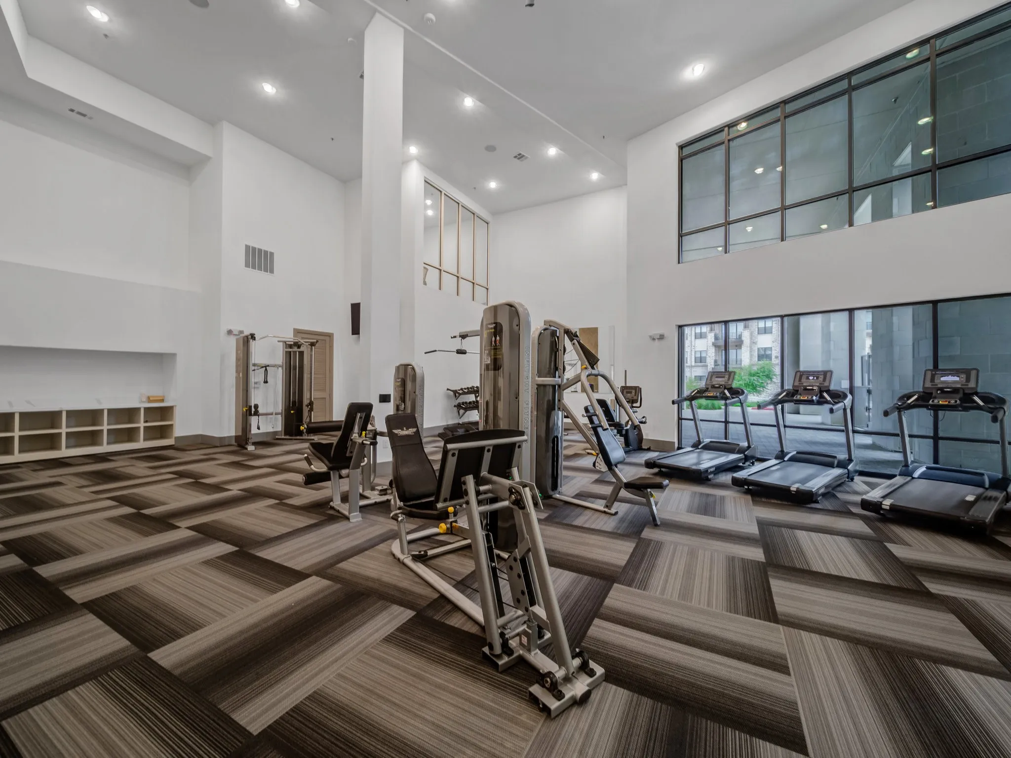 Fitness center featuring high ceilings, recessed lighting, expansive windows, modular carpet flooring, and integrated shelving