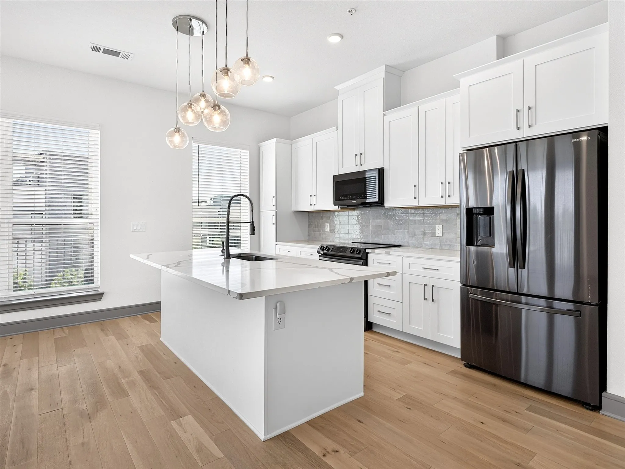 Kitchen featuring a central island with a sink, stainless steel appliances, white cabinetry, wood-finish flooring, and pendant lighting