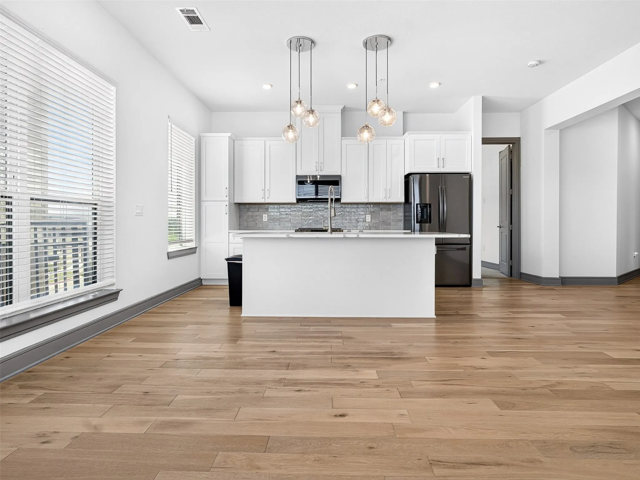 Kitchen featuring white cabinetry, a central island, stainless steel appliances, wood-finish flooring, and pendant lighting