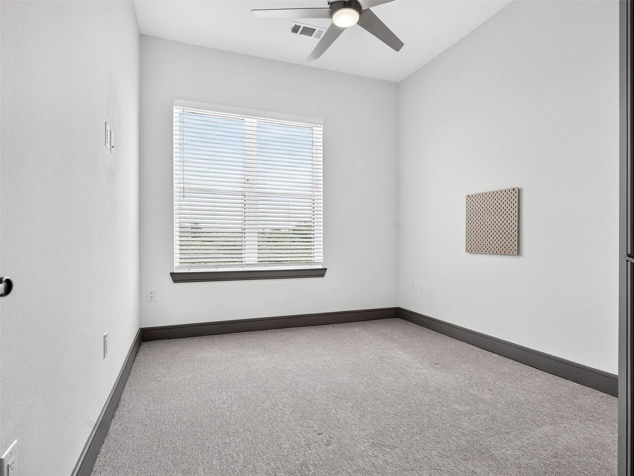 Carpeted room with a ceiling fan, window with blinds, and dark-toned trim
