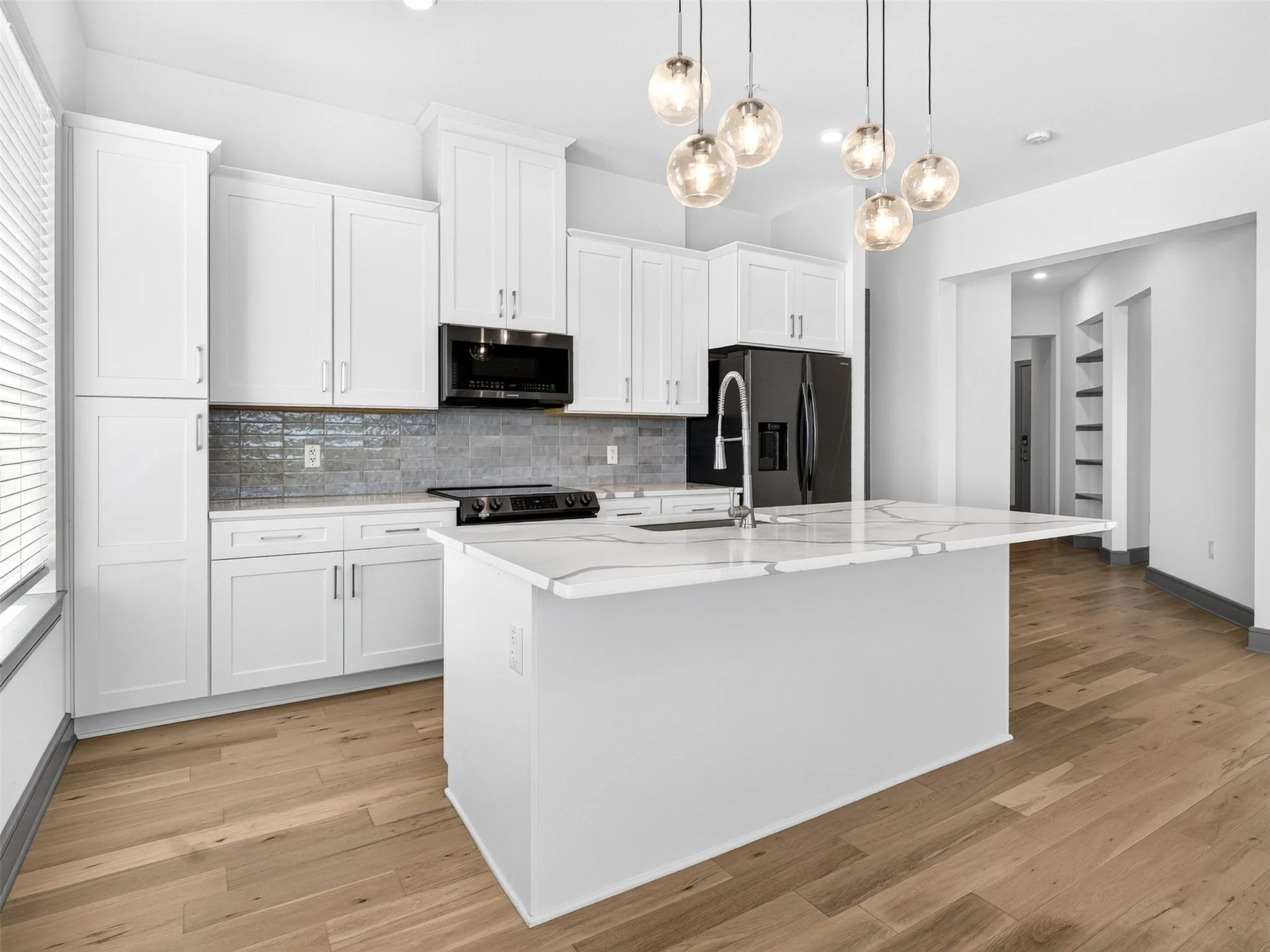 White cabinetry, light wood-finish flooring, island with a white countertop, black appliances, and a gray tile backsplash