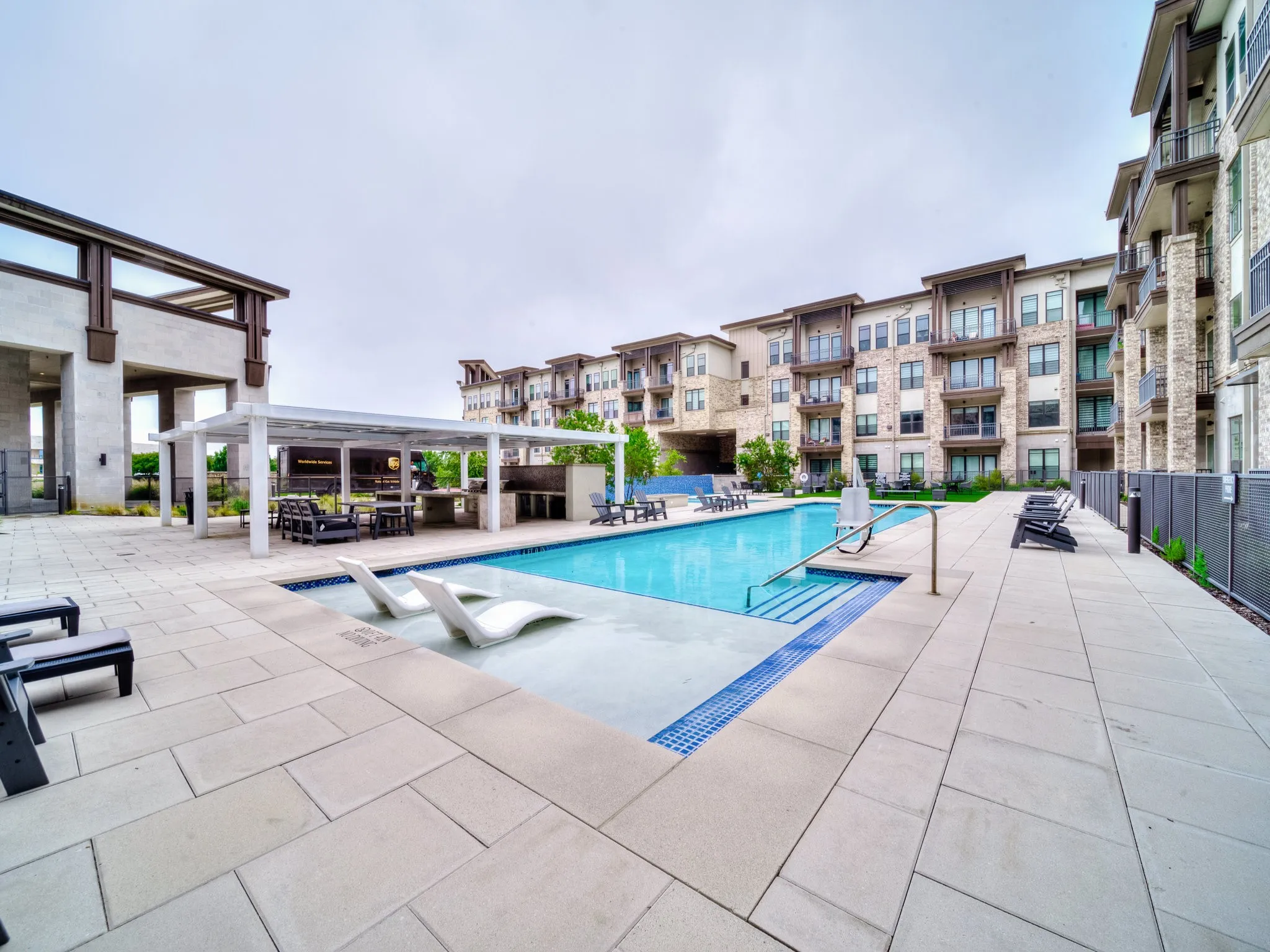 Expansive outdoor pool area featuring a rectangular pool, integrated lounge seating, and a shaded pergola with built-in grilling stations