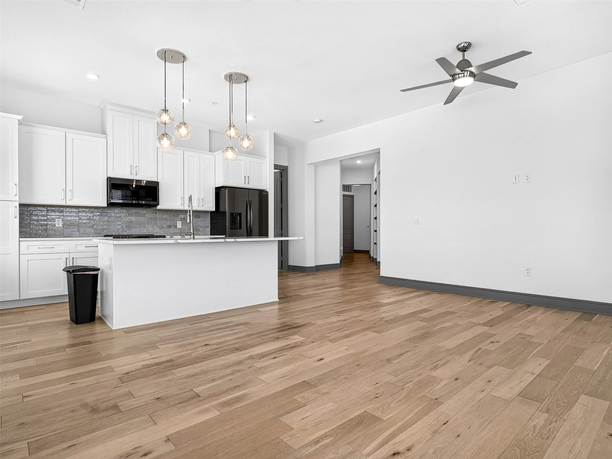 White shaker cabinetry, dark tile backsplash, a kitchen island with seating, pendant lighting, and wood-finish flooring