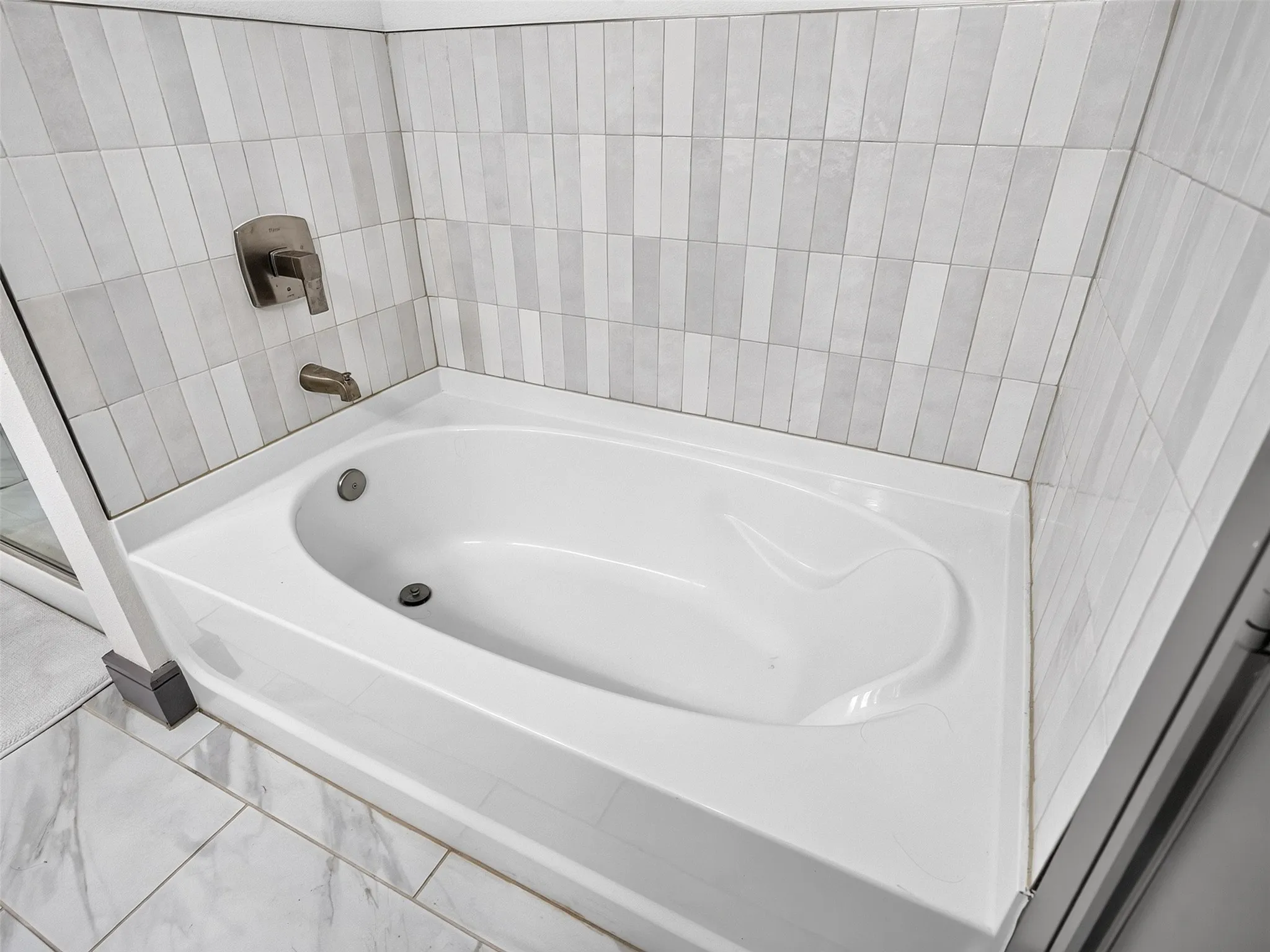 Built-in bathtub with a brushed nickel faucet and tile surround