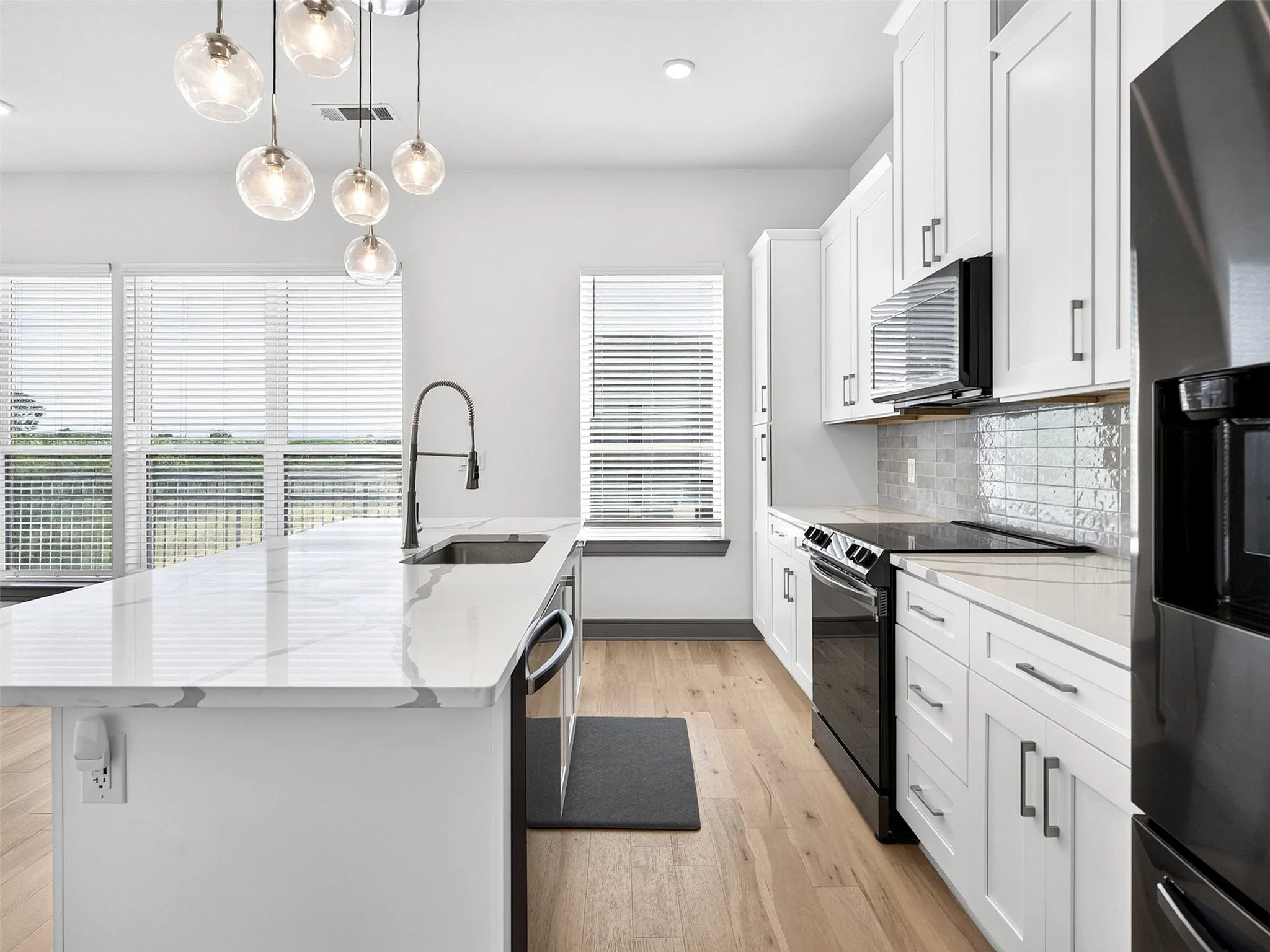 Kitchen featuring a quartz-finish island with an undermount sink, pendant lighting, wood-finish flooring, white cabinetry, and a tile backsplash