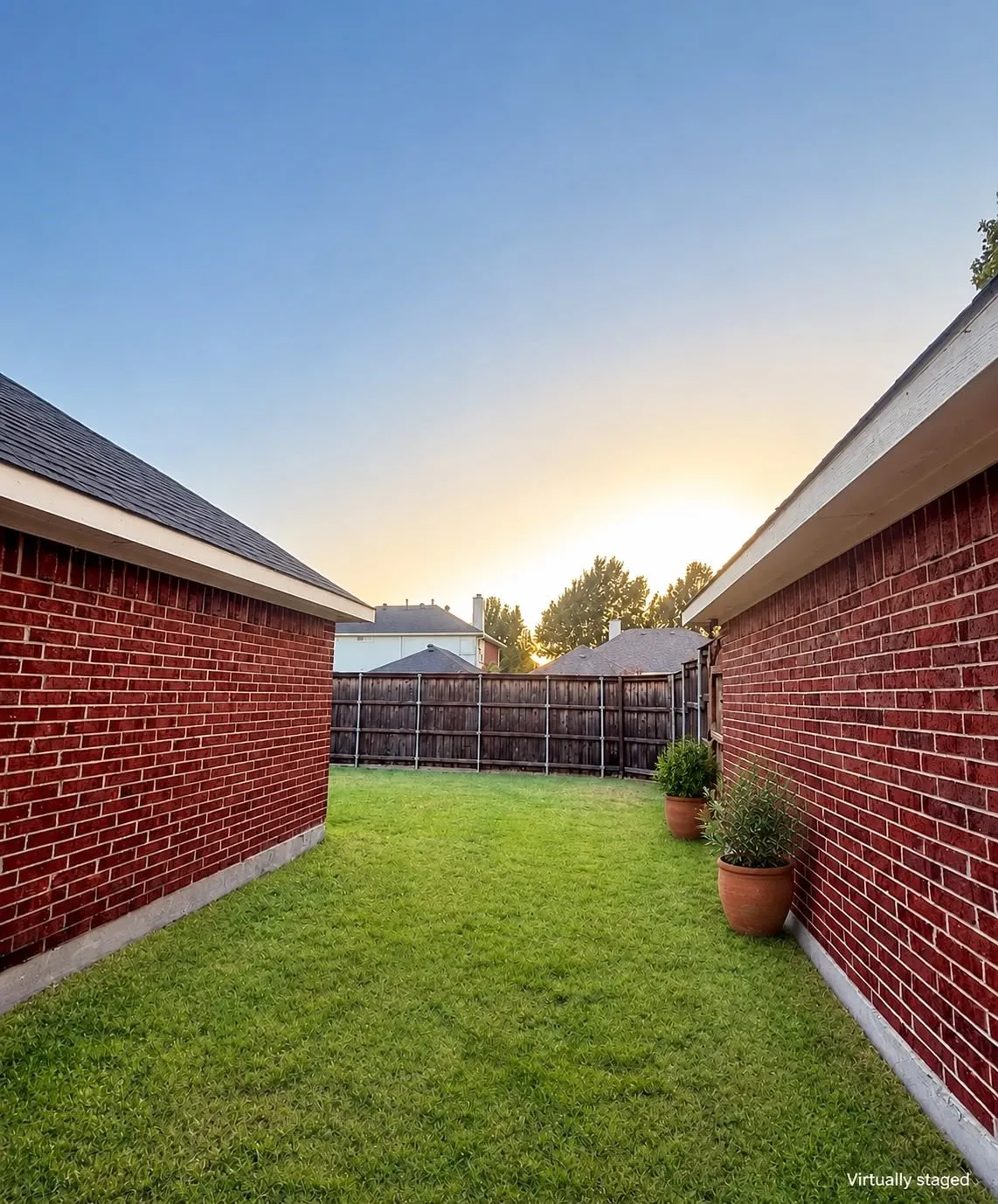 Fenced backyard with expansive green lawn, brick exterior walls, and a wood privacy fence