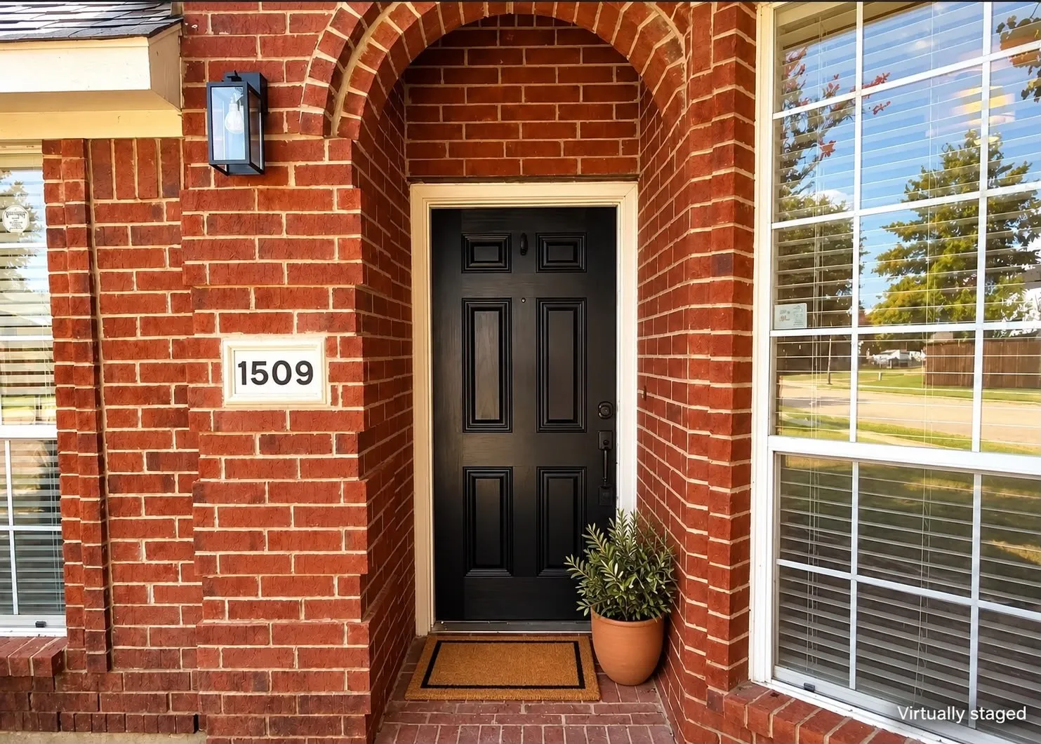 Red brick exterior with an arched entryway, recessed black paneled door, and an exterior light fixture