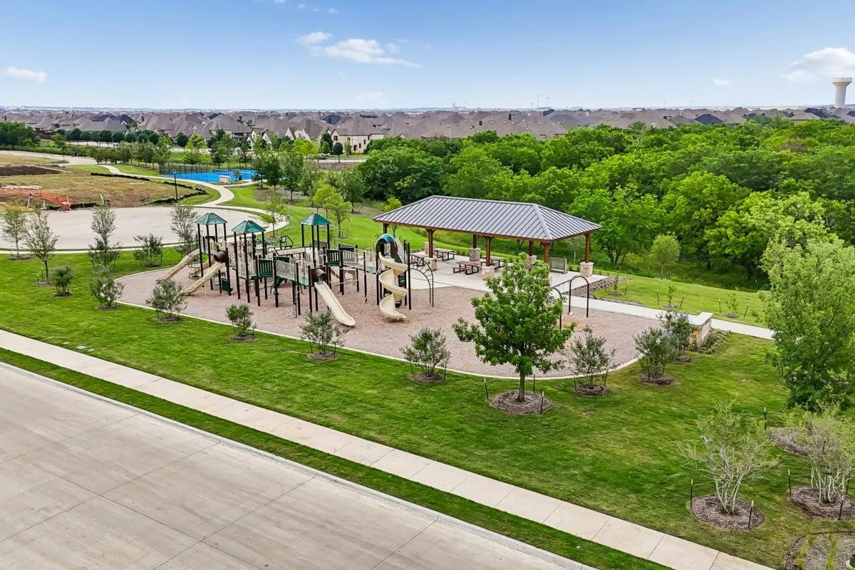 Expansive green space featuring a playground, shaded picnic area, winding pathways, and mature trees