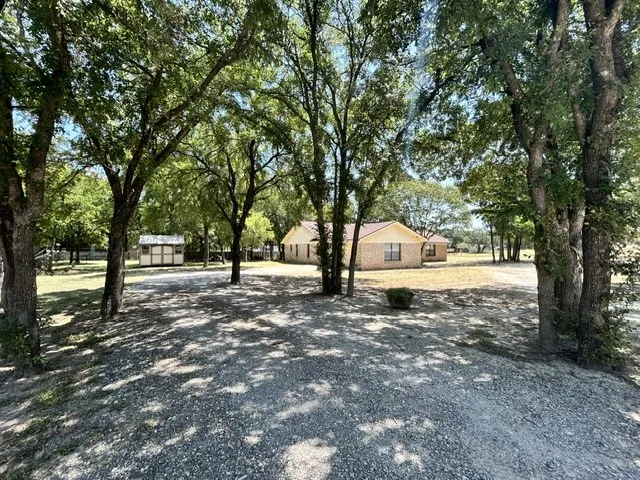 First driveway view with lots of shade, leading to the attached two car garage and storage shed.