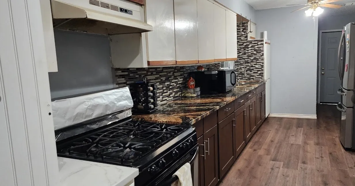 Wood-finish flooring, dark wood-finish base cabinetry, light-colored upper cabinetry, mosaic tile backsplash, and a gas range