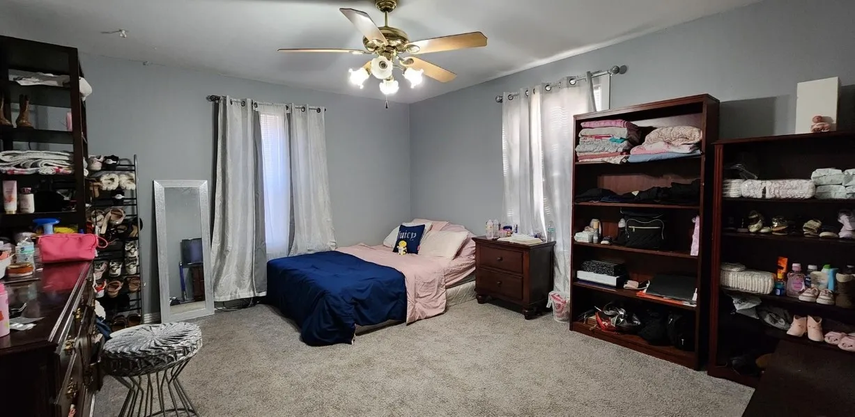 Carpeted room with a ceiling fan, two windows with curtain rods, and painted walls