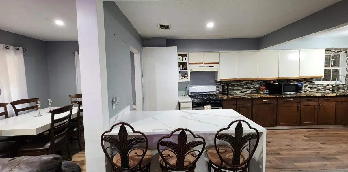 Kitchen featuring a large island with a light-toned countertop, wood-finish flooring, and a decorative tile backsplash