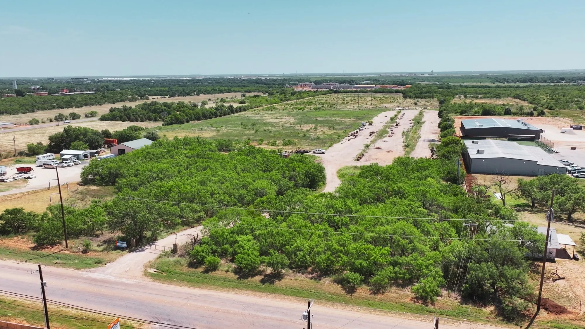 Expansive property featuring a paved road frontage, natural tree coverage, open land, and multiple structures
