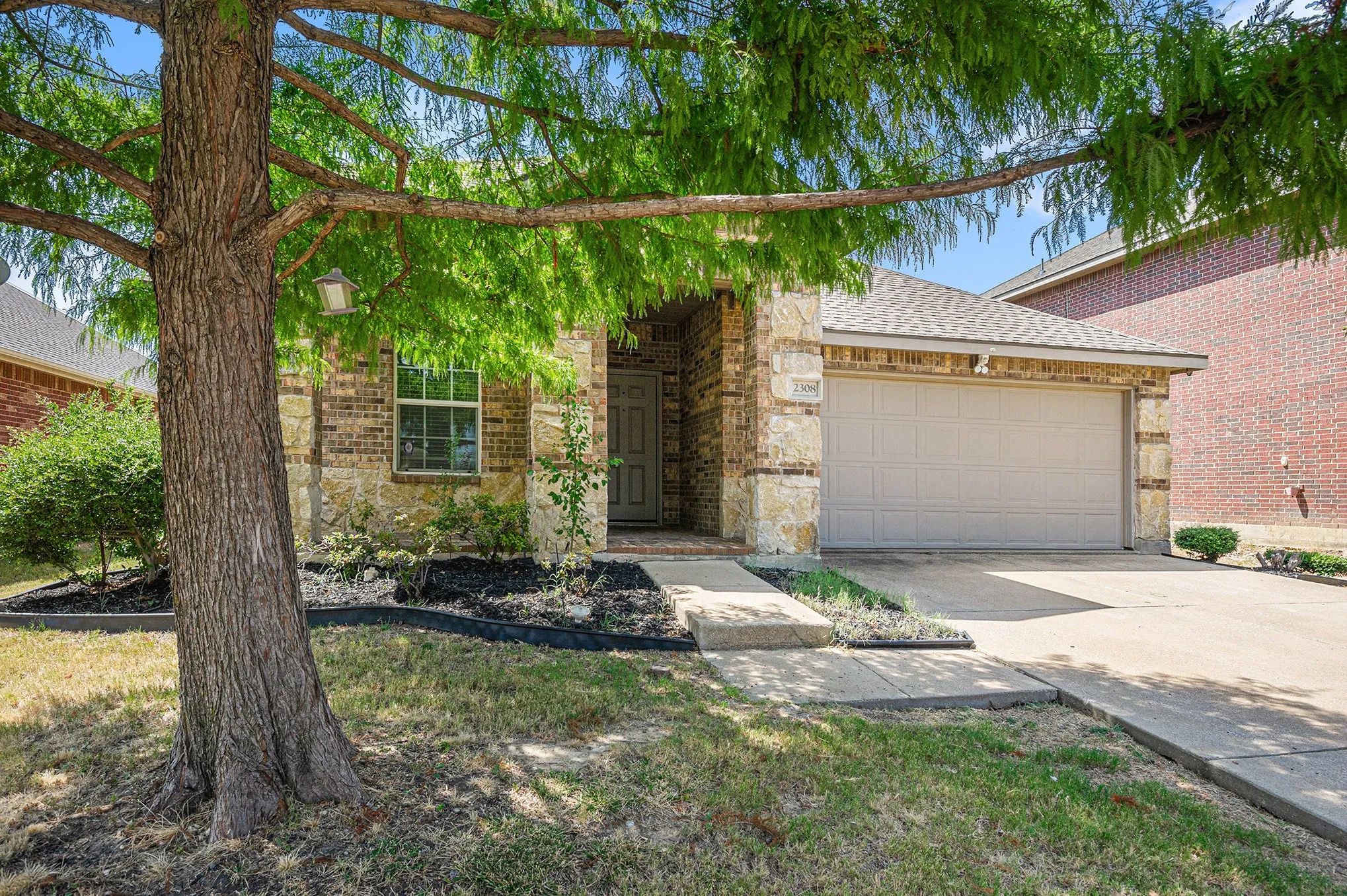View of front of house featuring an attached garage, a shingled roof, driveway, and brick siding