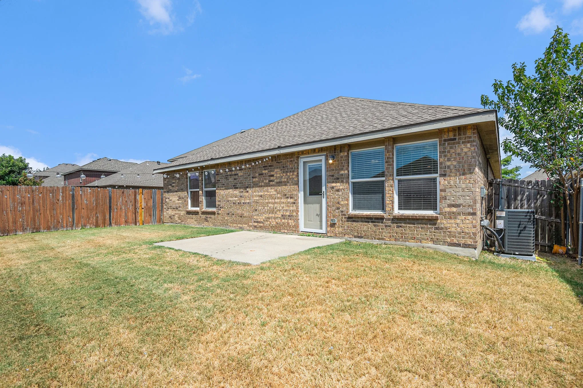 Rear view of house with a patio, a fenced backyard, brick siding, and roof with shingles