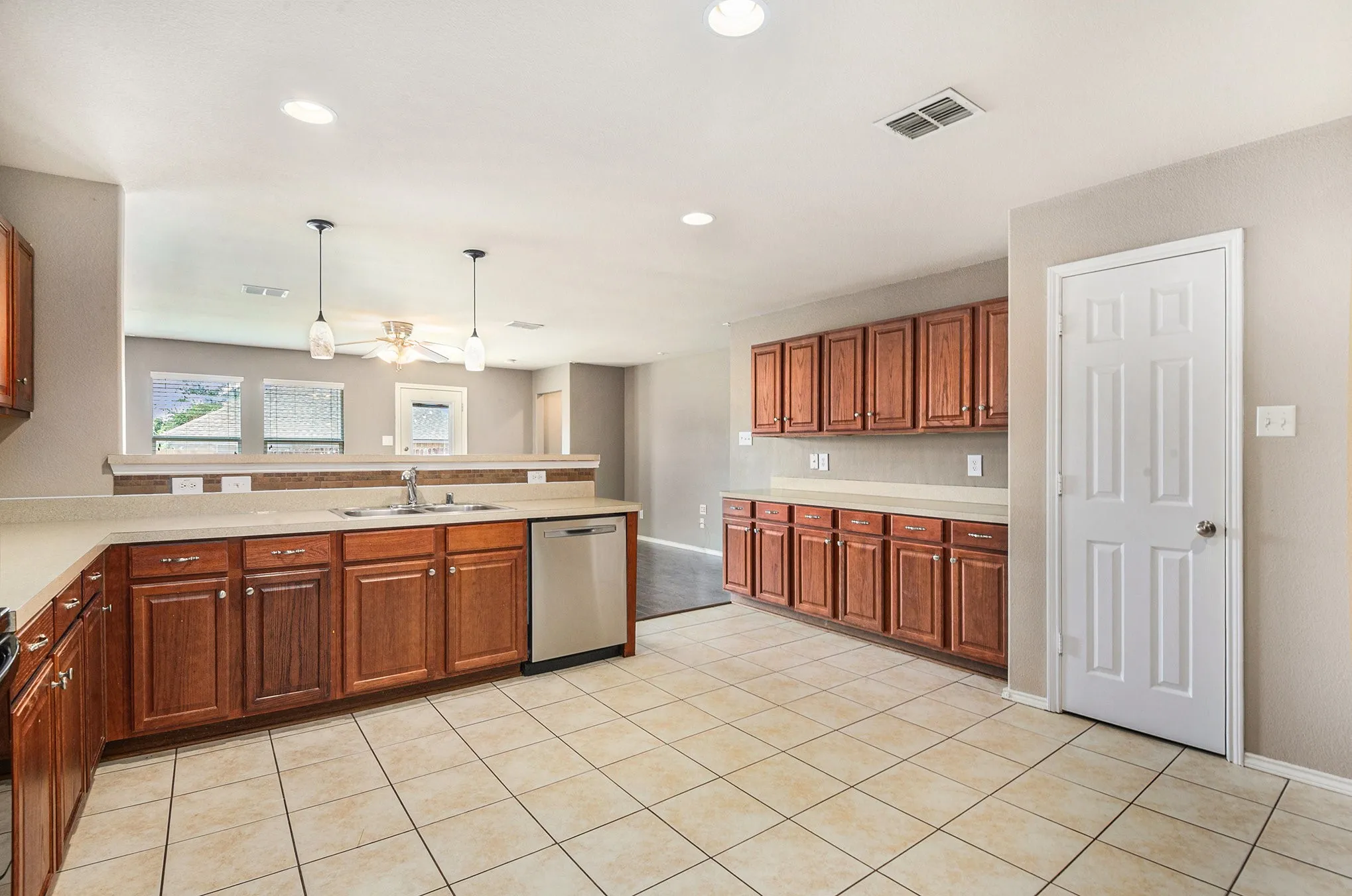 Kitchen featuring light tile patterned floors, brown cabinetry, light countertops, stainless steel dishwasher, and recessed lighting