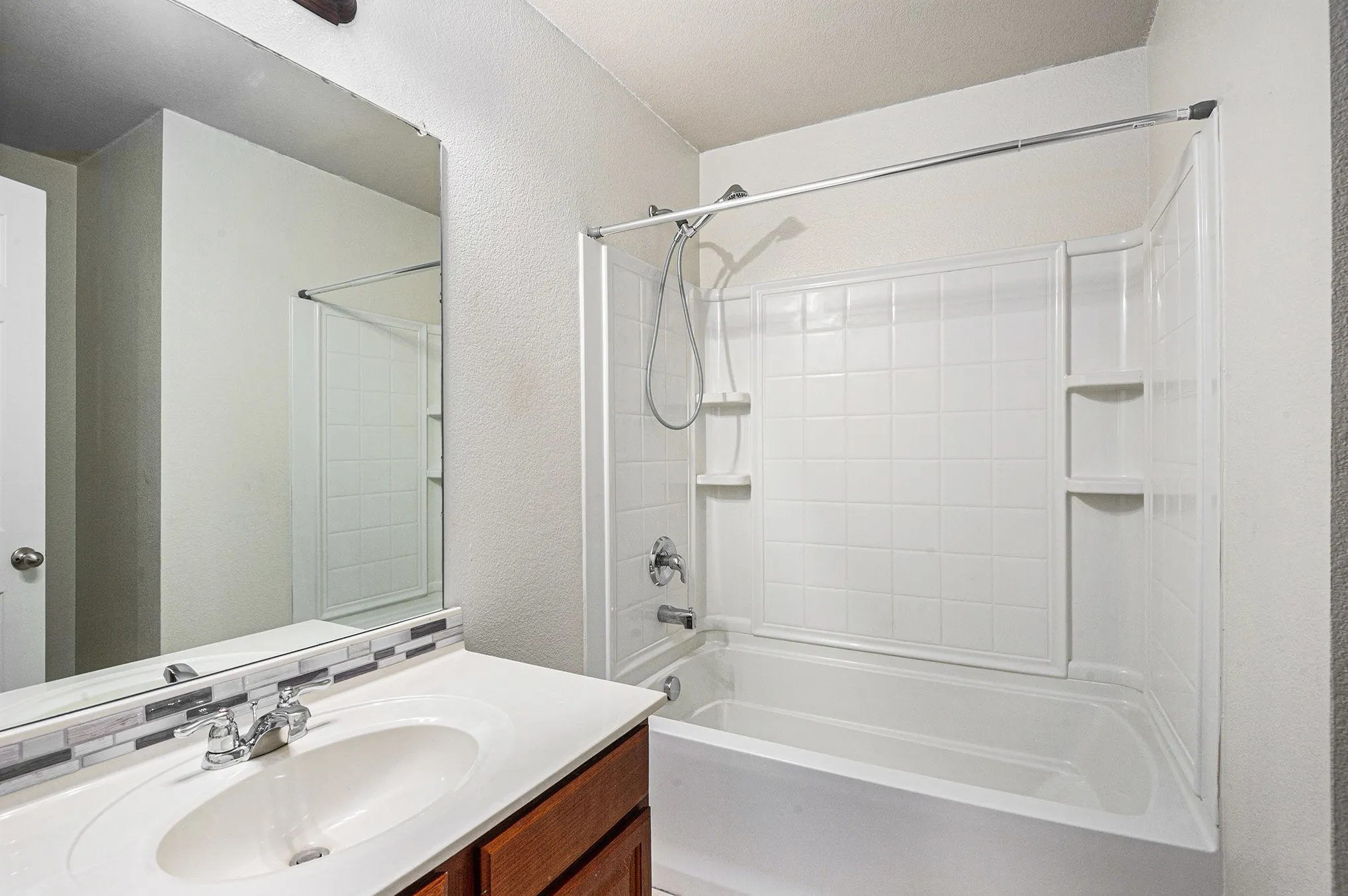 Full bathroom featuring a textured wall,  shower combination, and vanity
