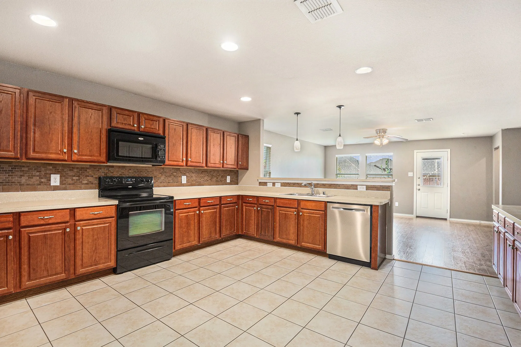 Kitchen with black appliances, a peninsula, hanging light fixtures, light tile patterned flooring, and recessed lighting